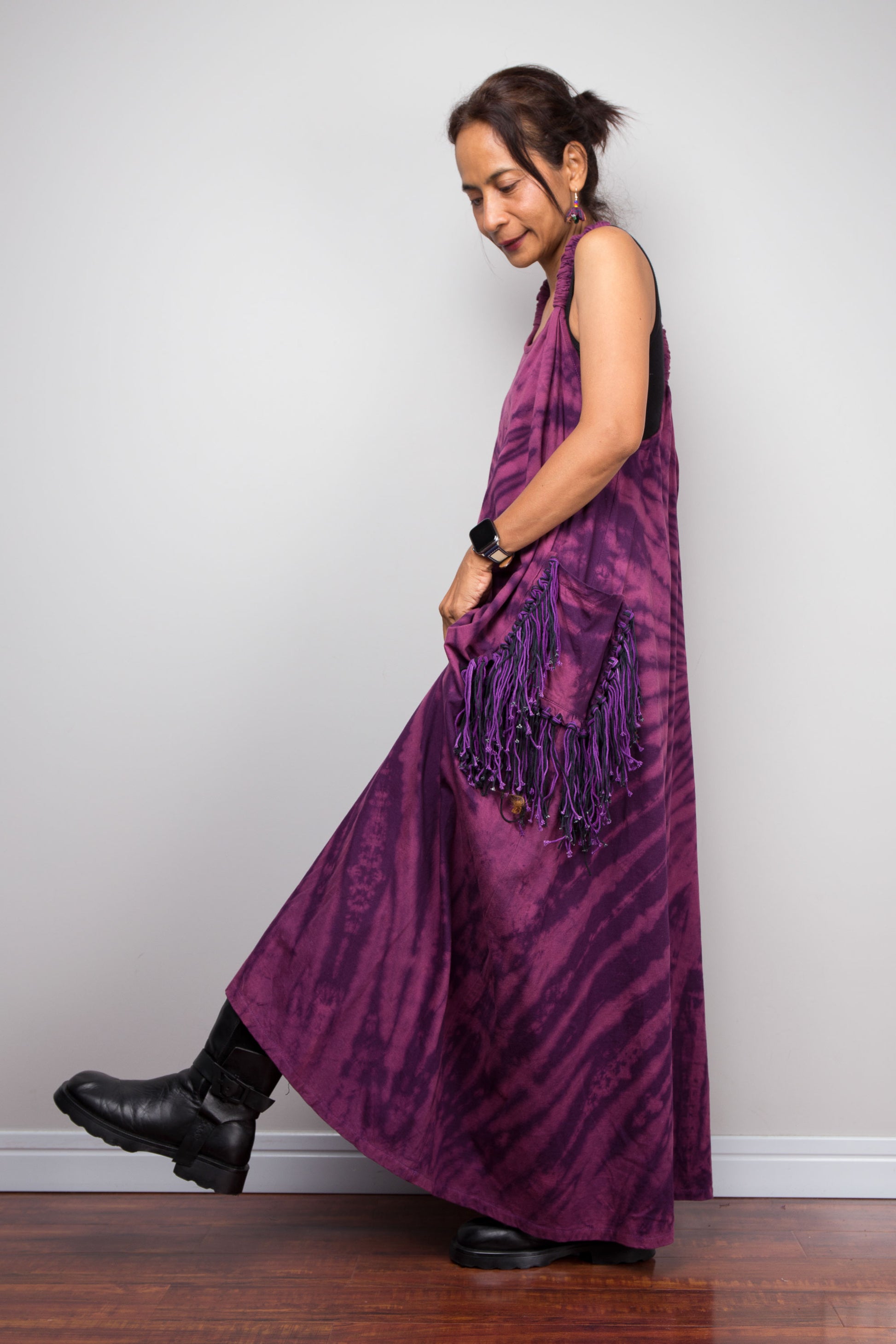 Side view of a model wearing the Nuichan purple tie dye sleeveless maxi dress, showcasing the tonal plum and magenta starburst pattern and purple yarn tassel patch pockets.
