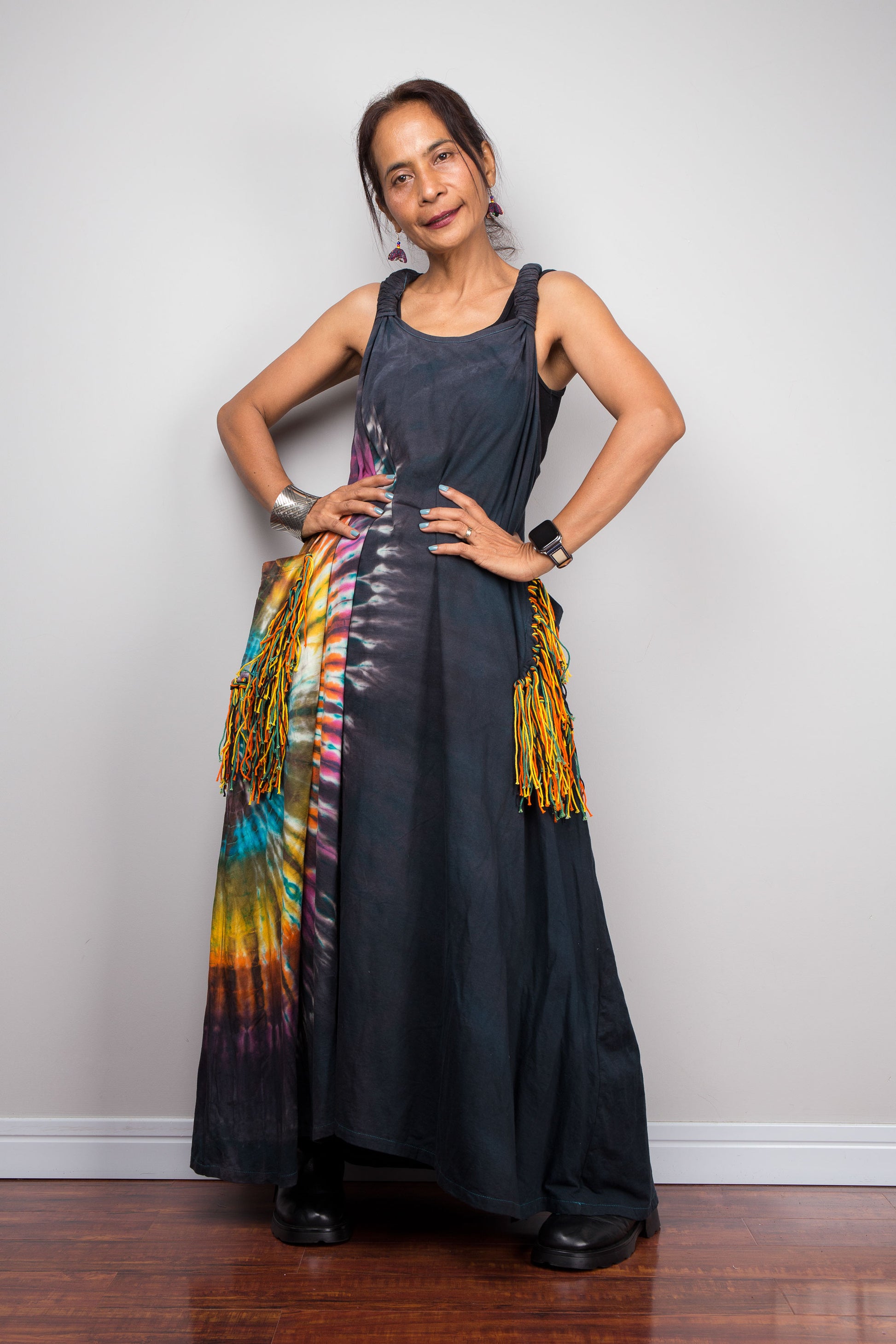 Front-facing view of a model wearing the Nuichan sleeveless tie-dye boho maxi dress, showing the scoop neckline, flowing A-line silhouette, and multicolour yarn fringe patch pockets on both hips.