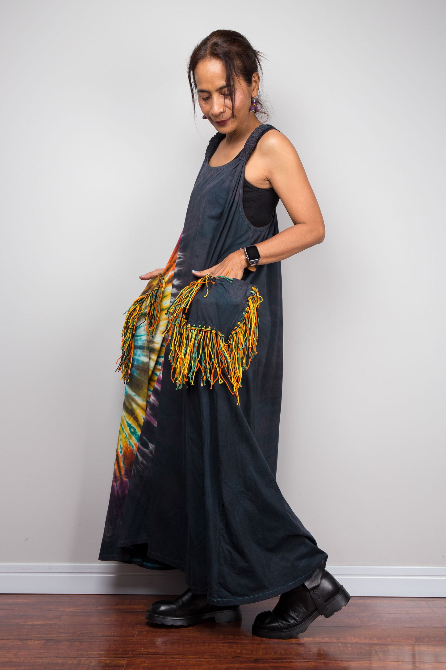 Side view of a model wearing the Nuichan sleeveless tie-dye boho maxi dress, showing the flowing A-line silhouette, and multicolour yarn fringe patch pockets on both hips.