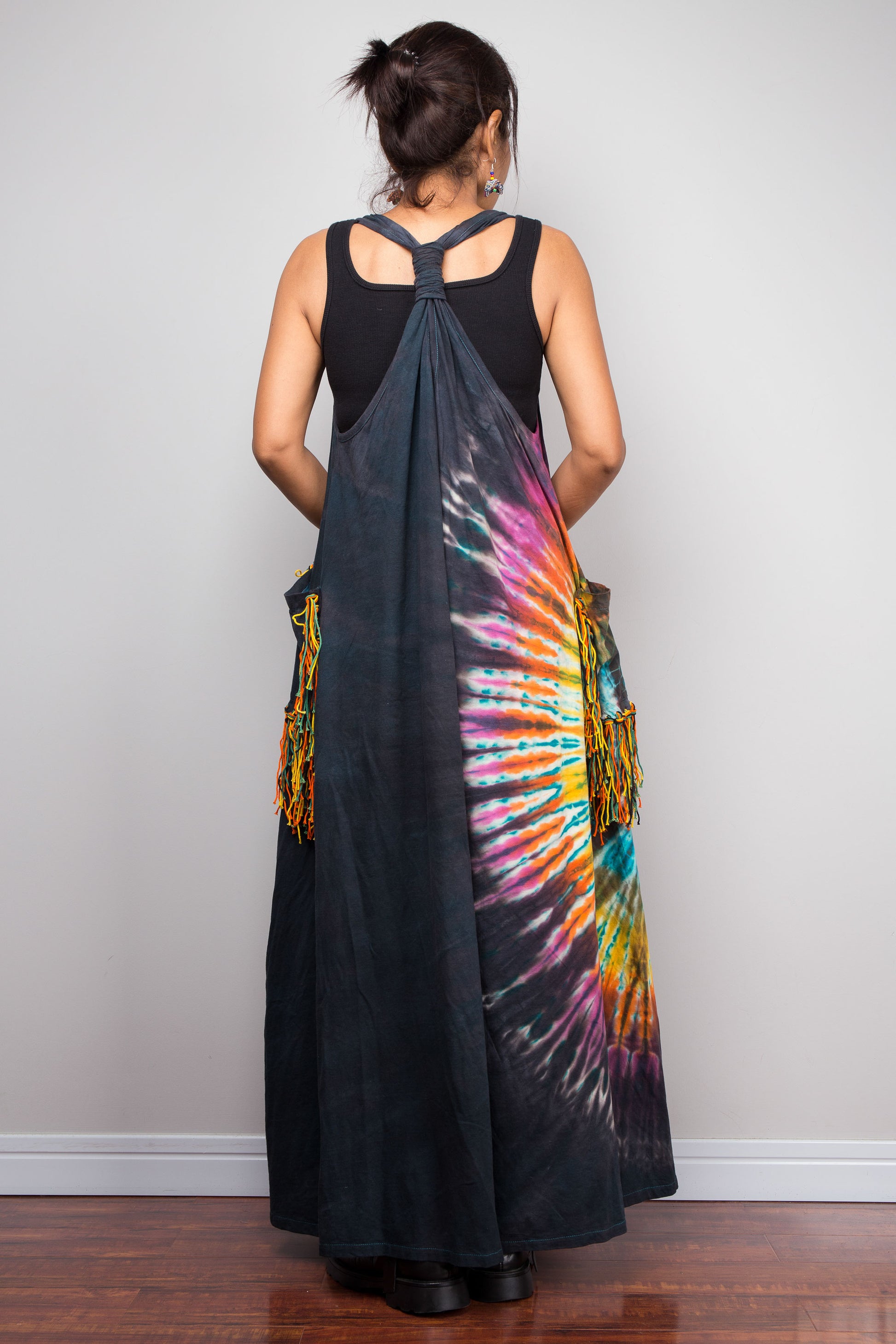 Rear view of a model in the Nuichan tie-dye festival maxi dress, highlighting the unique twisted macramé-style gathered back strap detail, dramatic sunburst print, and fringe tassel side pockets.