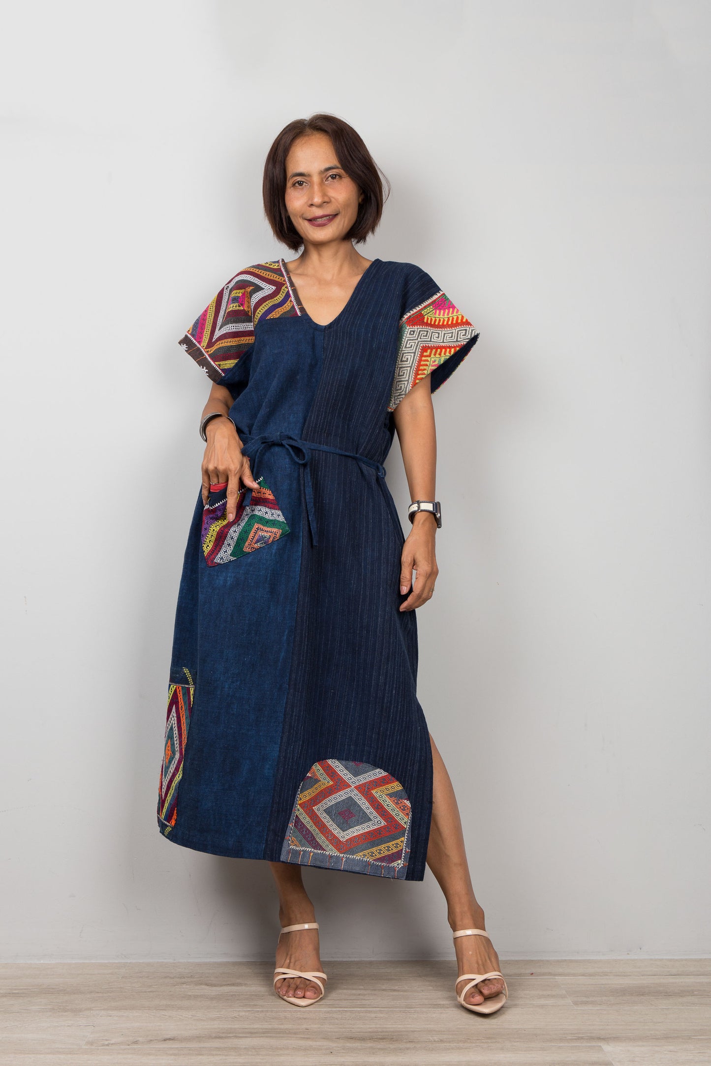 Woman wearing a blue cotton dress (great for petites women) with colorful geometric, embroidered patterns on a plain background