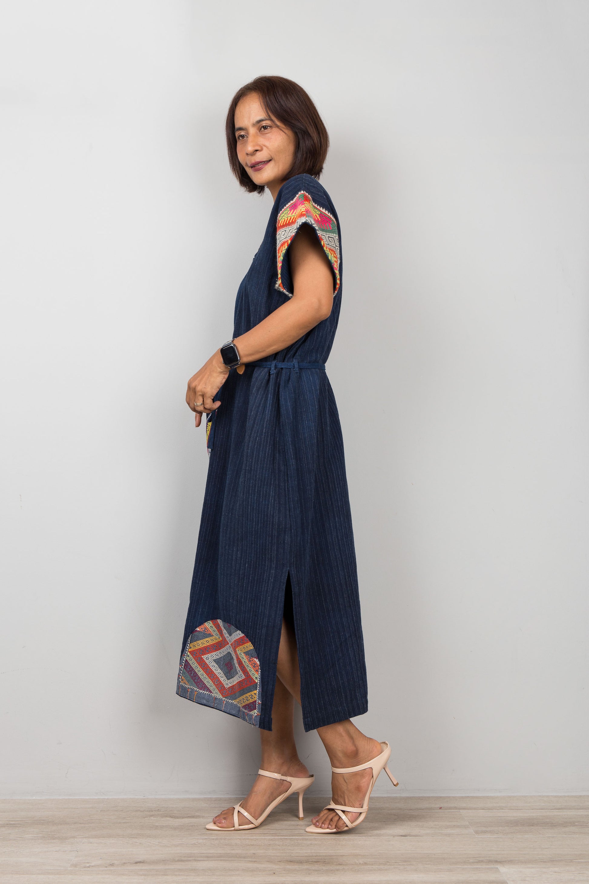 Woman wearing a blue cotton patchwork midi dress with colorful patterns on a plain background