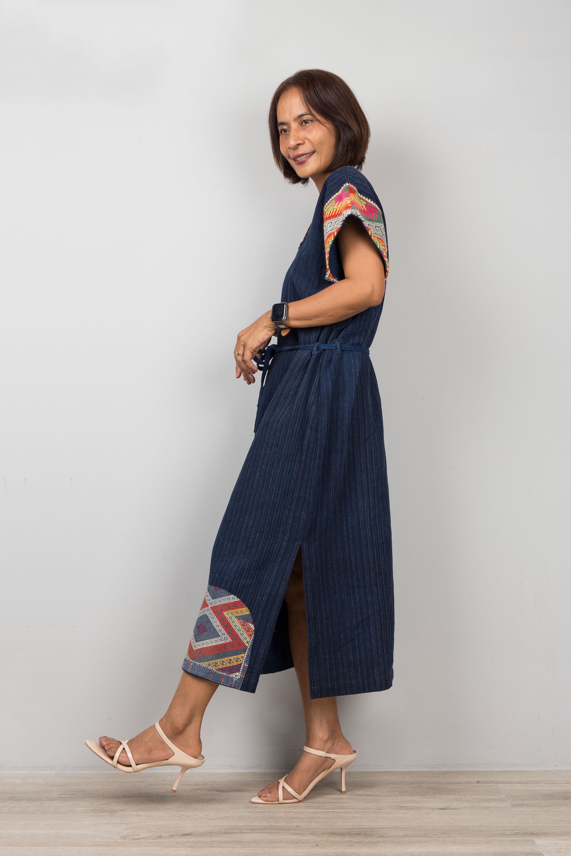Woman wearing a blue cotton patchwork dress with colorful patterns on the sleeves against a white background