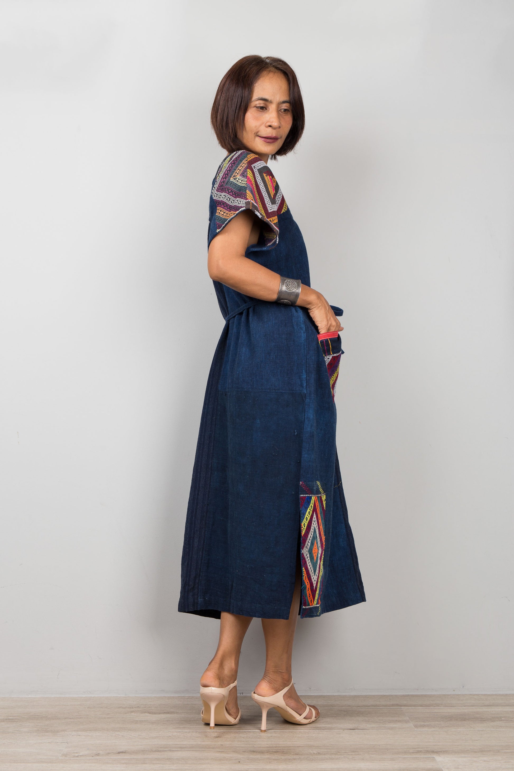 Woman wearing a blue dress with colorful patterns on a plain background