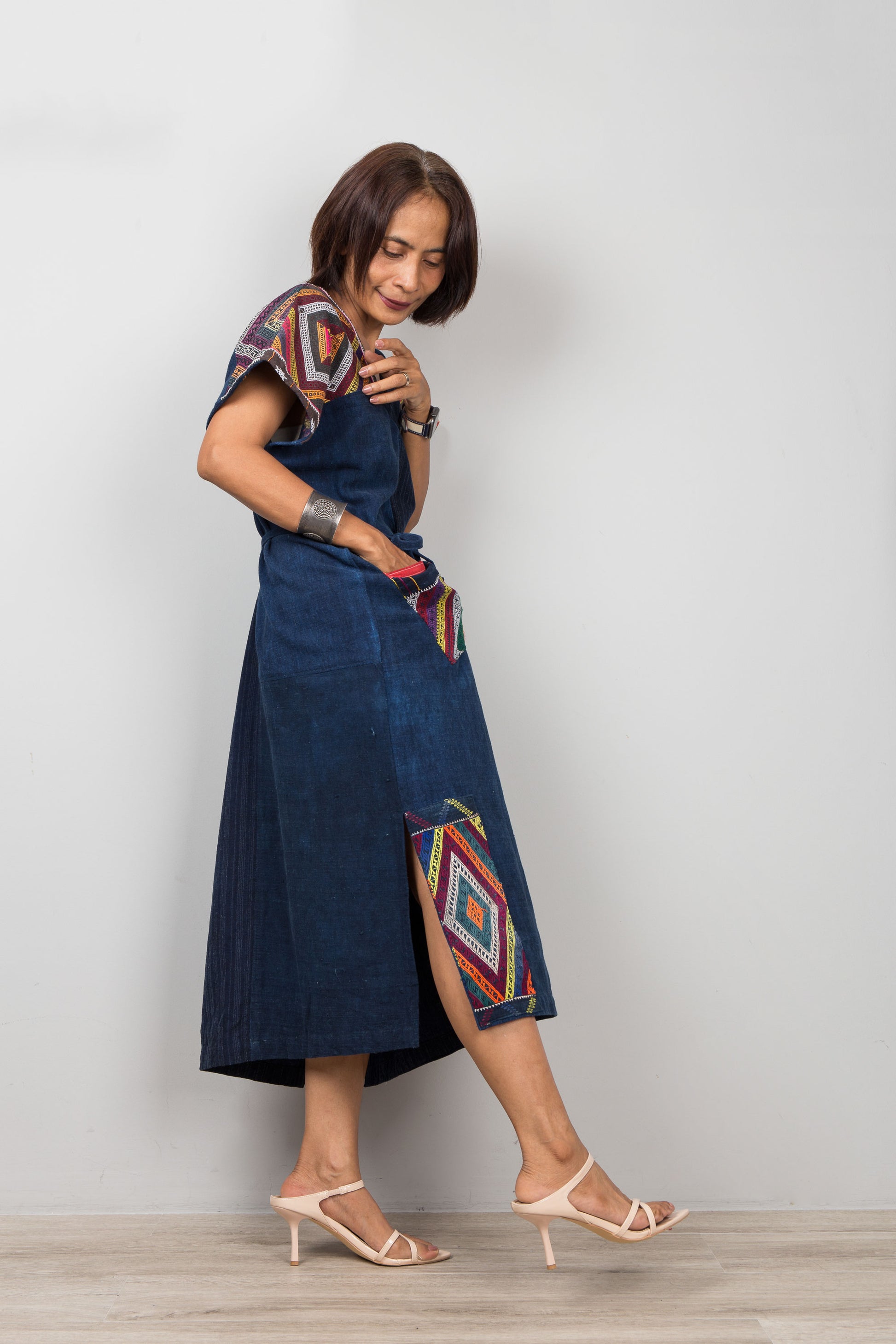 Nuichan wearing a blue cotton patchwork dress with colorful geometric embroidered patterns on a plain background