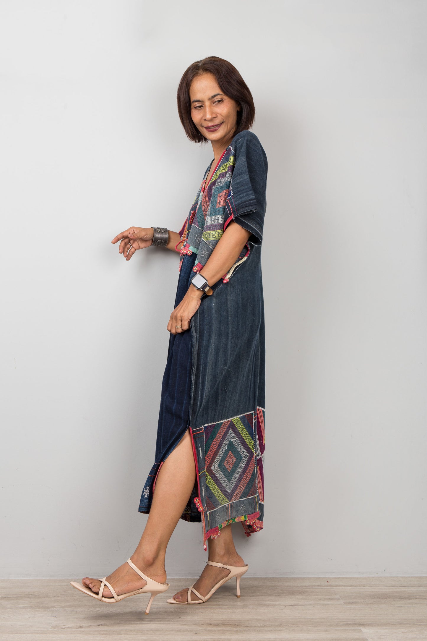 Woman wearing a long, dark blue dress with colorful patterns on a plain background