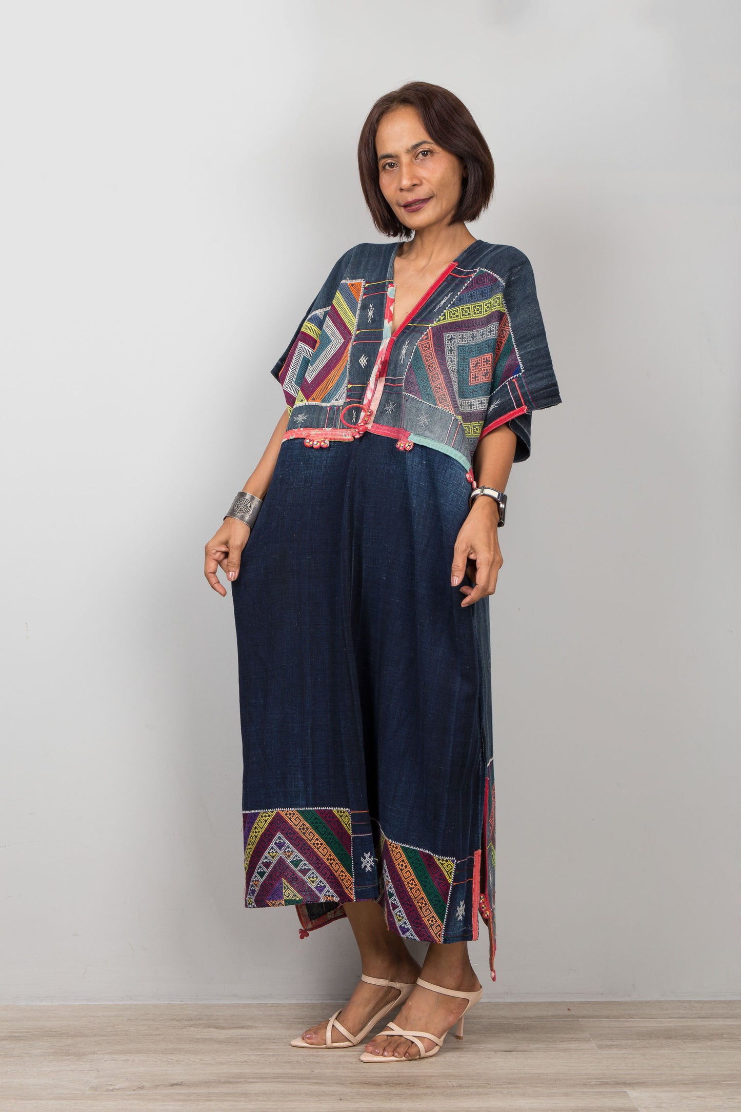 Woman wearing a colorful embroidered top and navy pants against a plain background