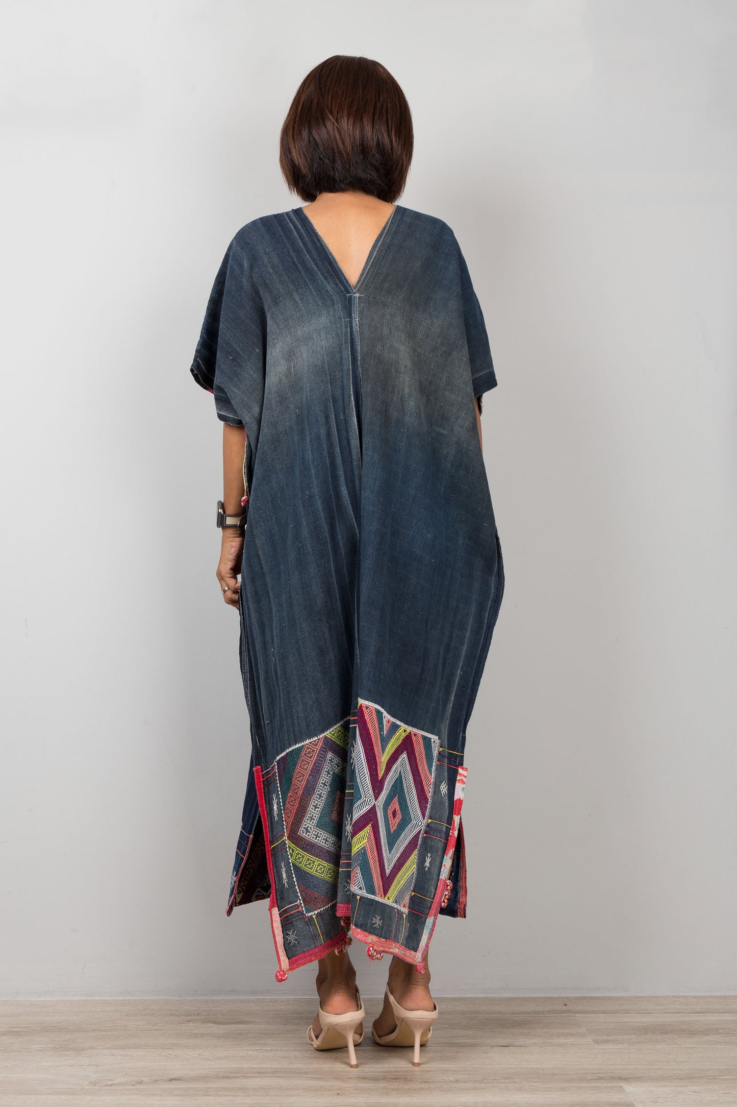Woman wearing a long, dark blue dress with colorful patterns on the hem against a plain background