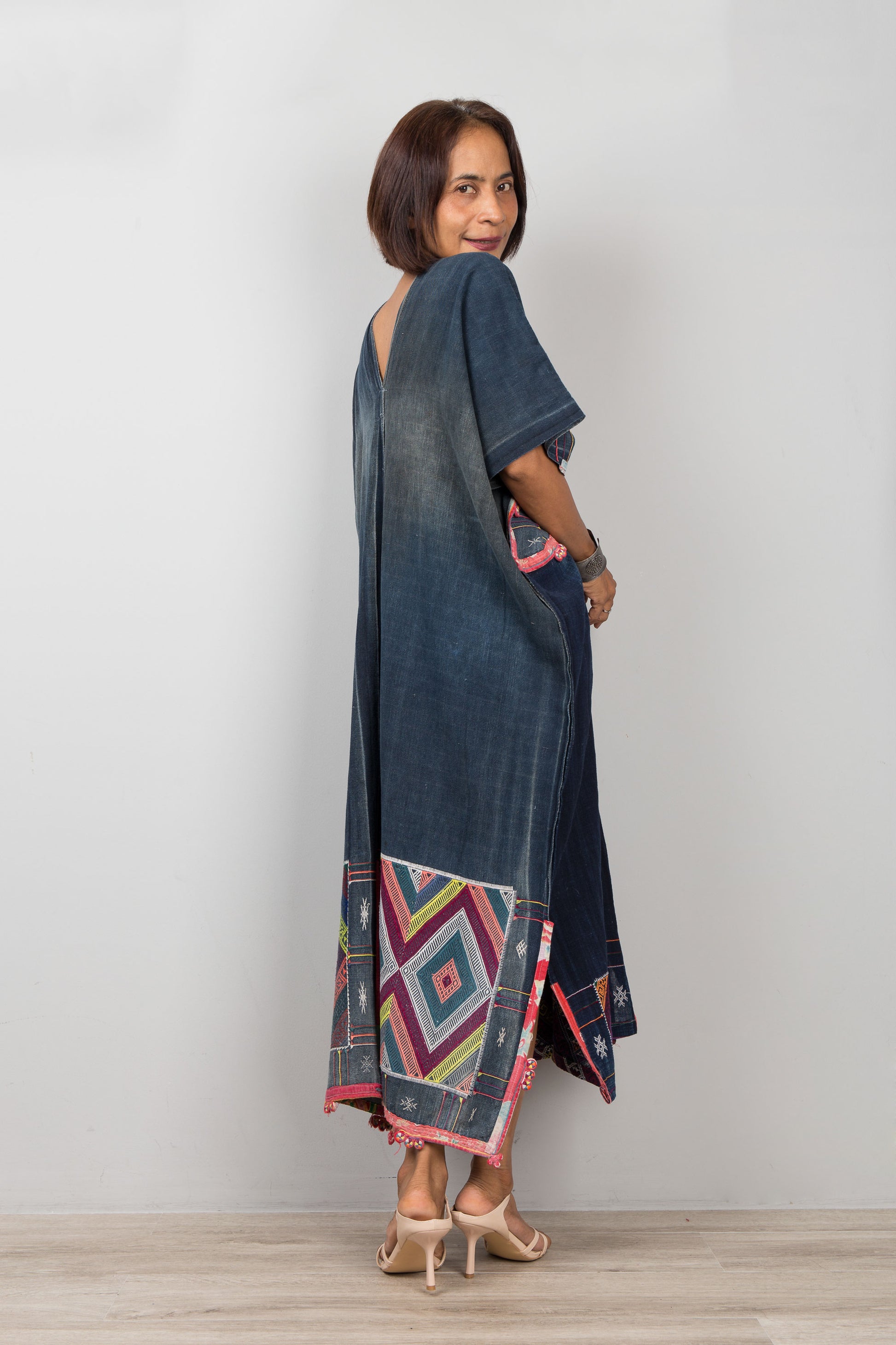 Woman wearing a long, dark blue dress with geometric patterns on a plain background