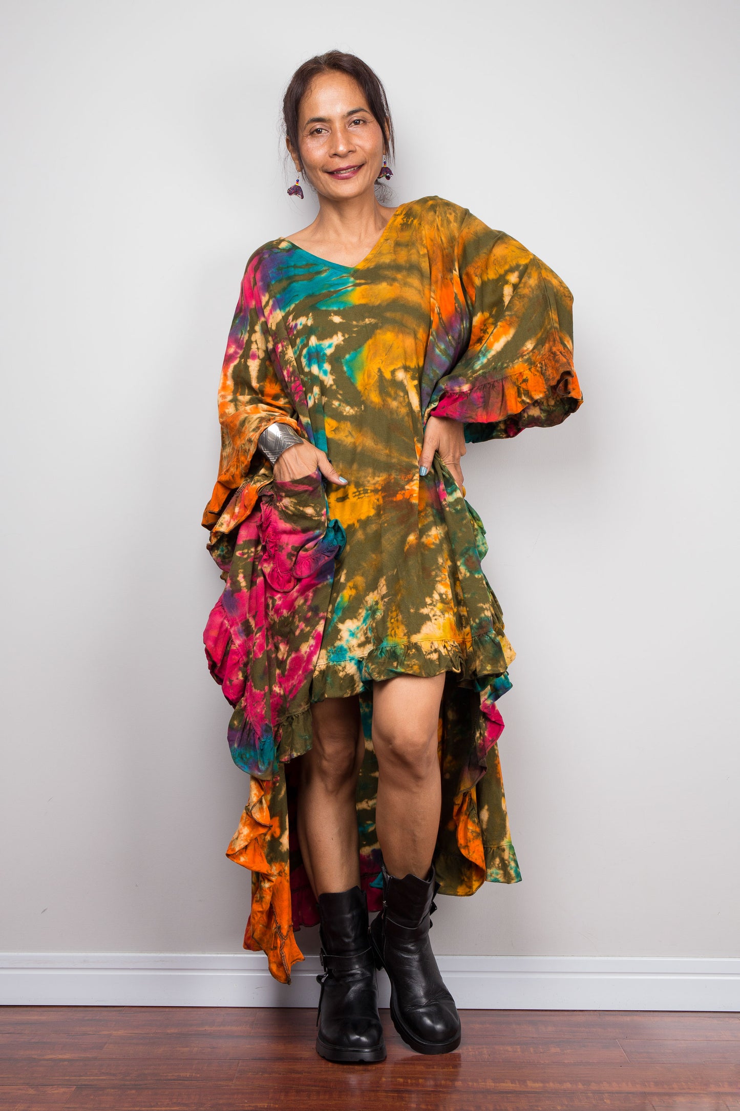 Woman wearing a colorful tie dye caftan tunic dress with ruffled sleeves against a plain background