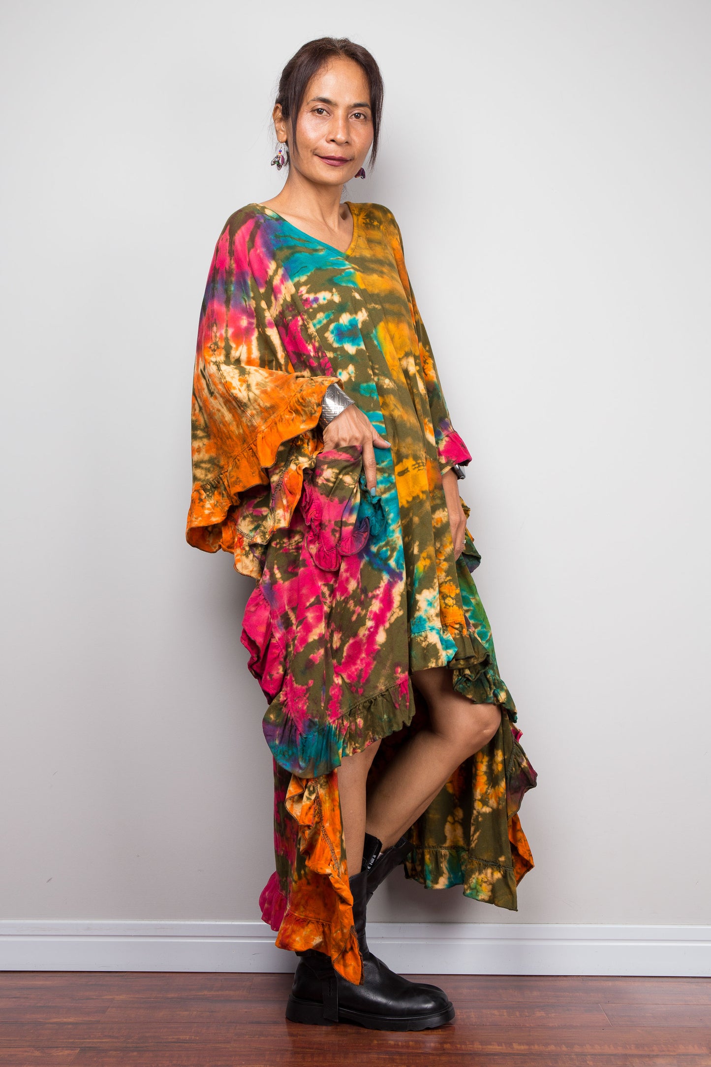 Petite Woman wearing a colorful, tie dye caftan tunic dress with a front pocket, against a white wall.
