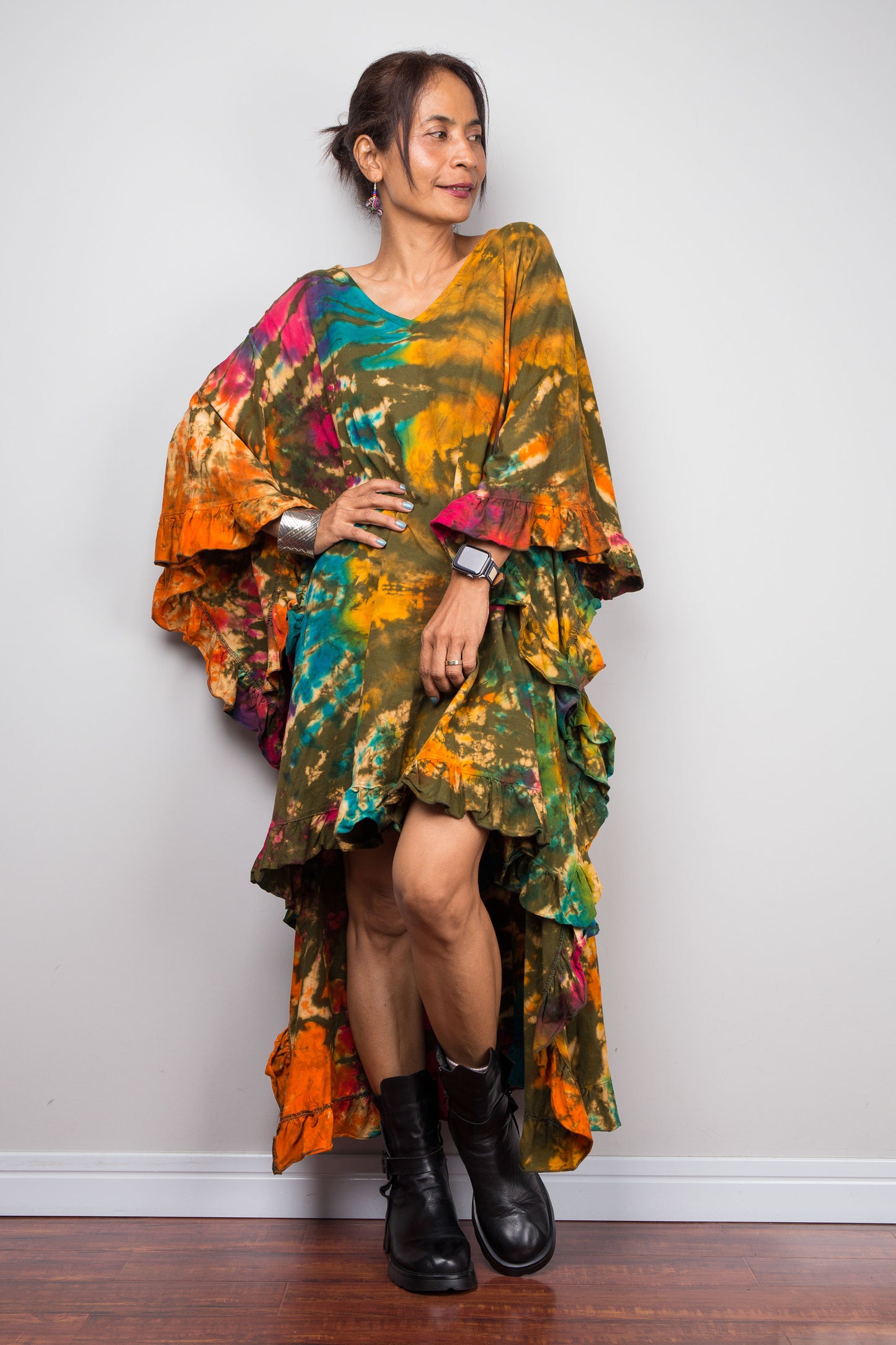 Woman wearing a colorful tie dye caftan tunic dress with a patterned design against a white wall.