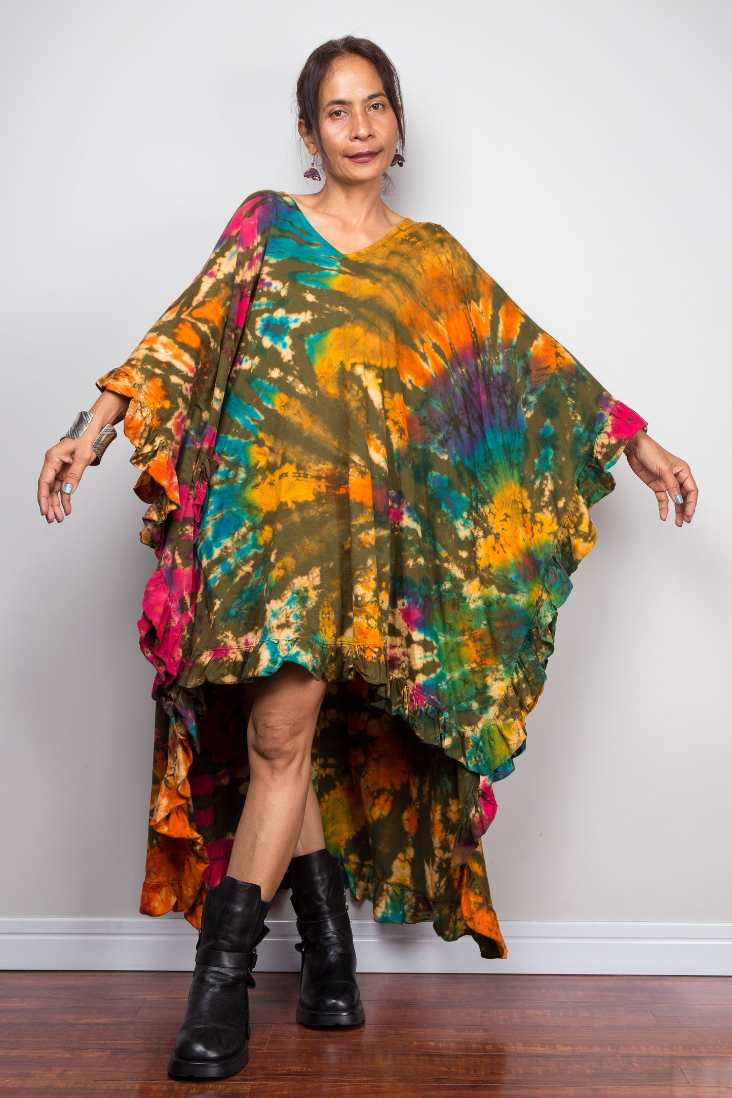 Woman wearing a colorful loose fit tie-dye caftan tunic dress with black boots on a plain background