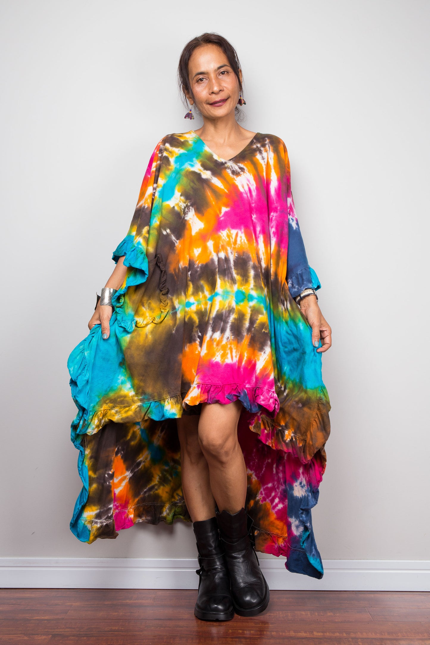 A petite woman wearing an original Nuichan vibrant, multicolored tie-dye kaftan tunic with a high-low hemline that is short in the front and cascades into a long train at the back