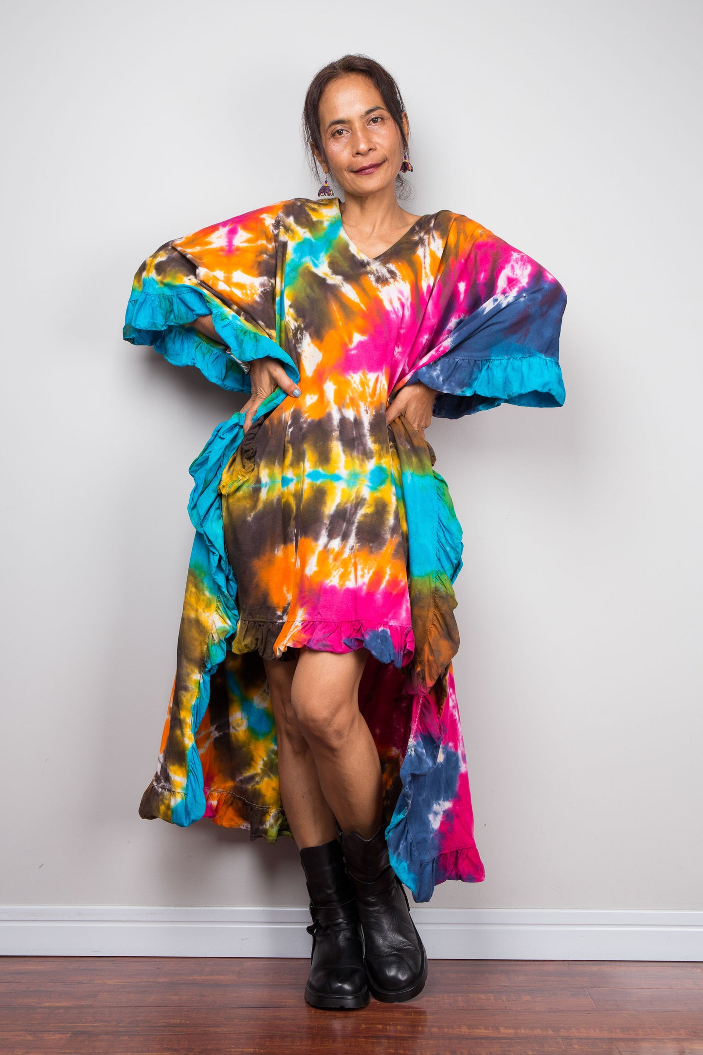 A petite woman wearing an original Nuichan vibrant, multicolored tie-dye kaftan tunic with a short front hemline that is short in the front and cascades into a long train at the back