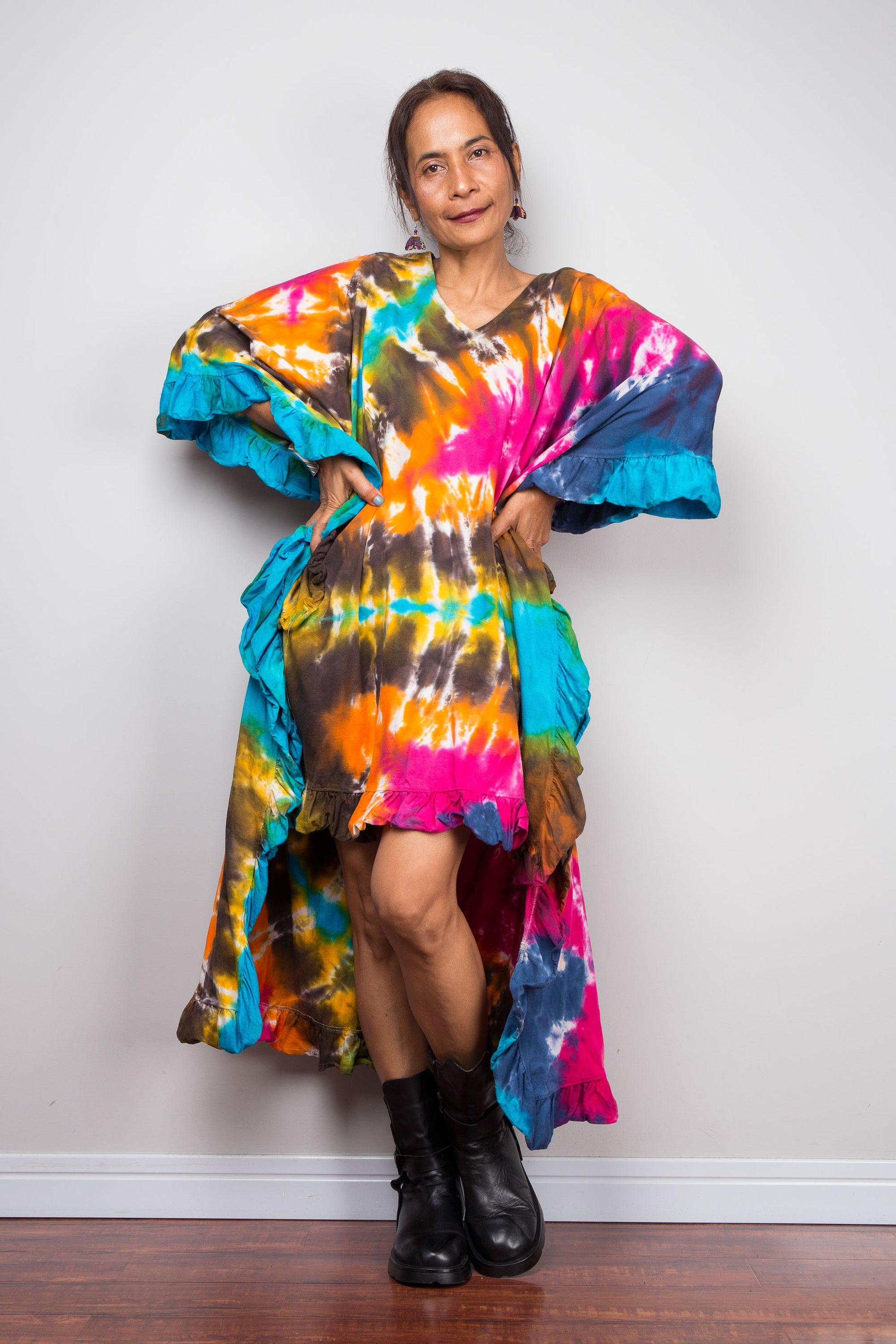 A petite woman wearing an original Nuichan vibrant, multicolored tie-dye kaftan tunic with a short front hemline that is short in the front and cascades into a long train at the back