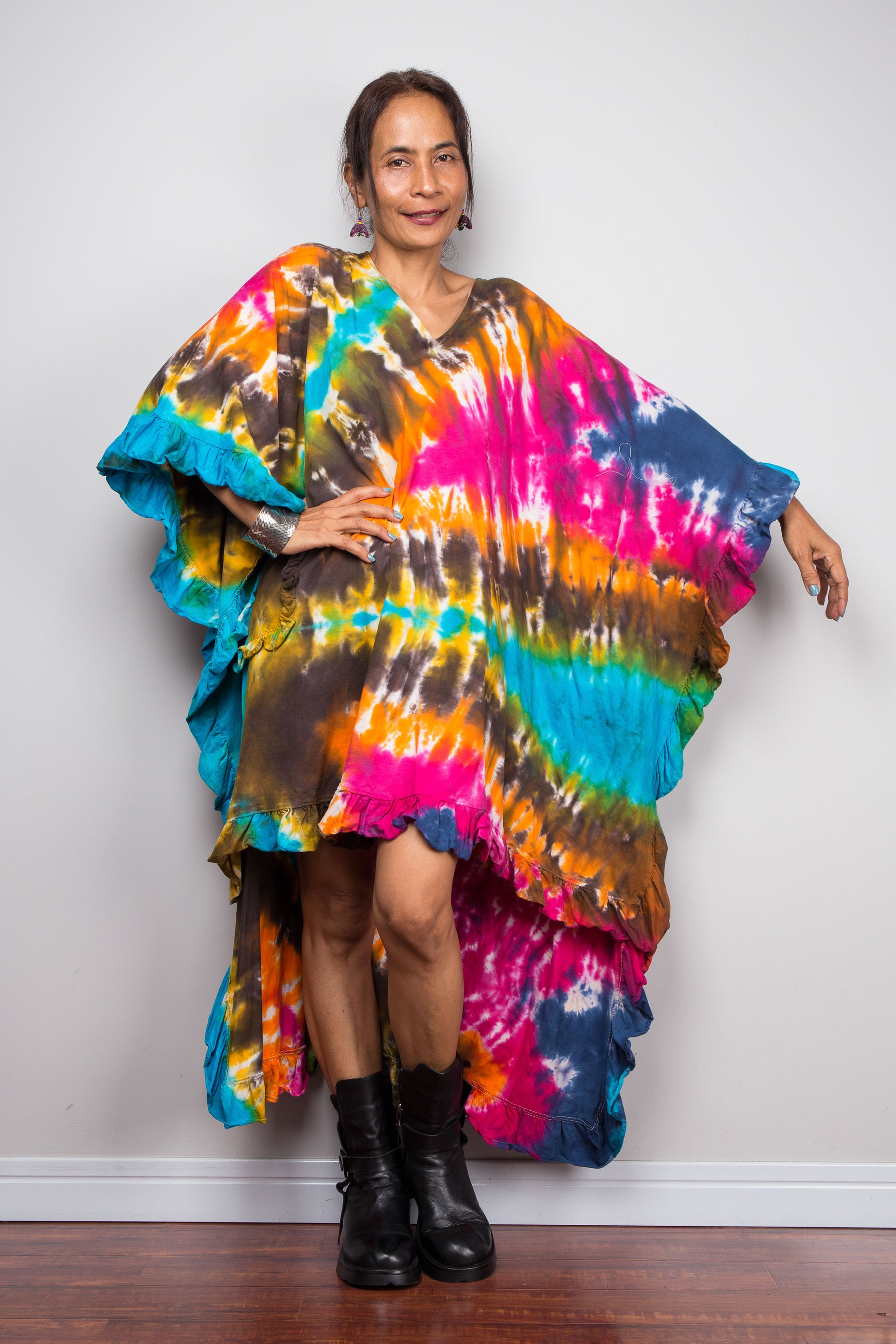A woman wearing a vibrant, multicolored tie dye caftan tunic with a high-low hemline that is short in the front and cascades into a long train at the back