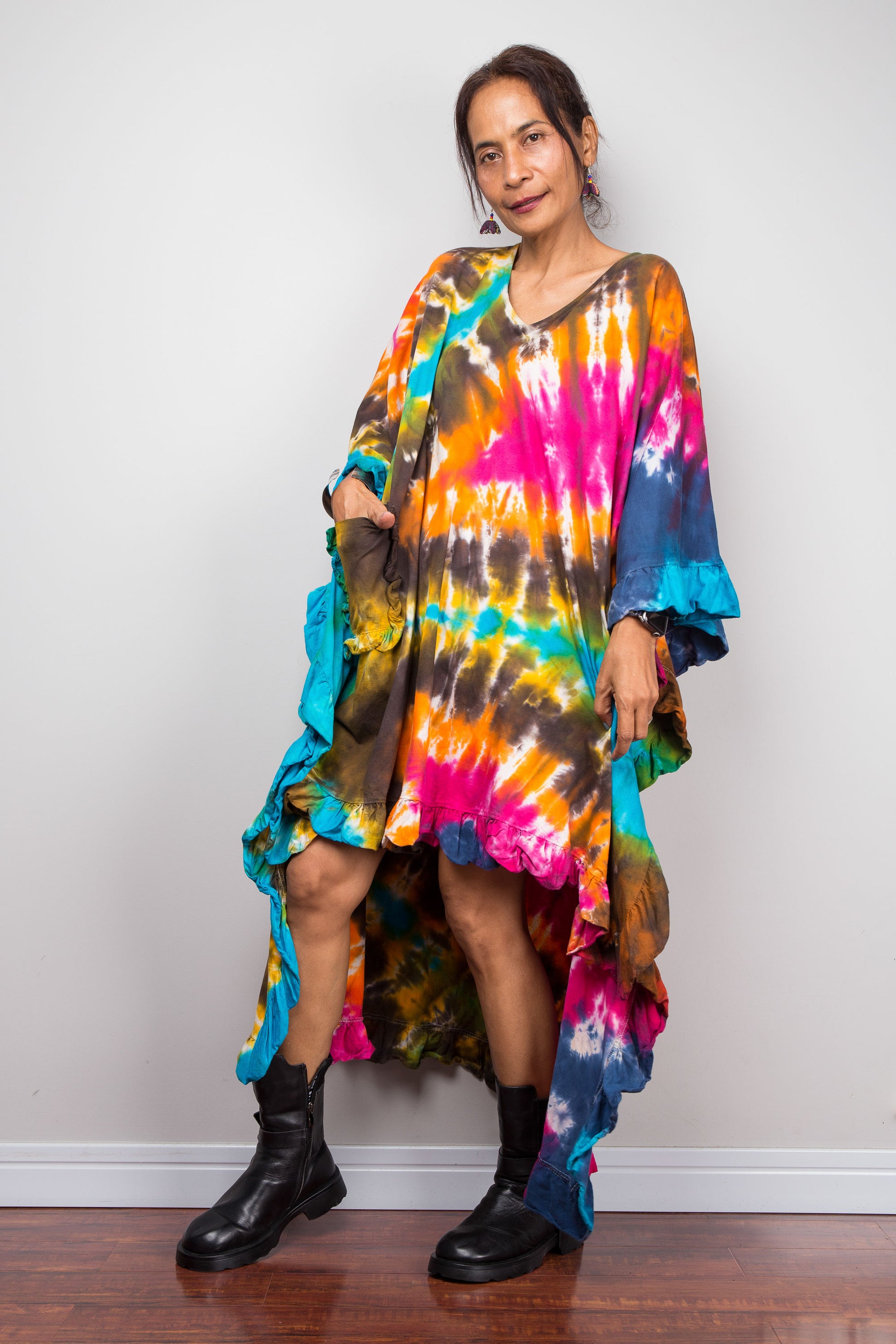 A woman wearing a vibrant, multicolored tie-dye kaftan tunic with a high-low hemline that is short in the front and cascades into a long train at the back, showing the front pocket