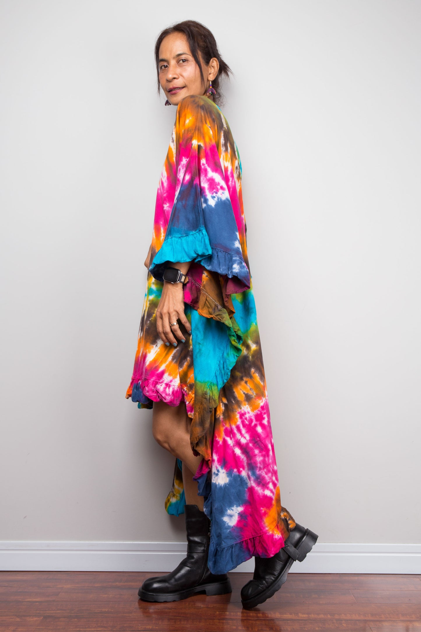 Side view of a petite woman wearing a vibrant, multicolored Nuichan tie dye kaftan tunic with a high-low hemline that is short in the front and cascades into a long train at the back