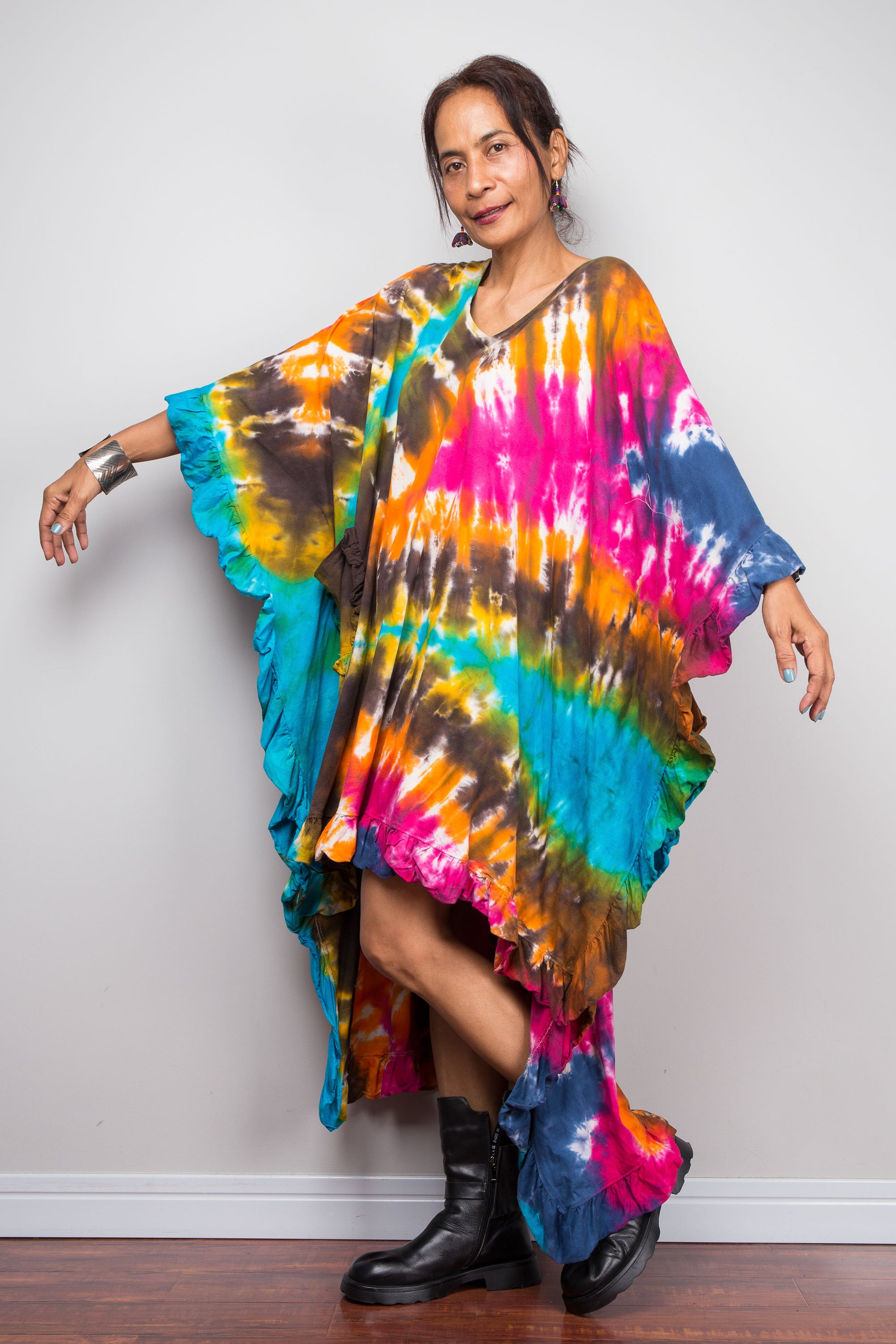 Side view of a woman wearing a vibrant, multicolored tie-dye kaftan tunic with a high-low hemline that is short in the front and cascades into a long train at the back