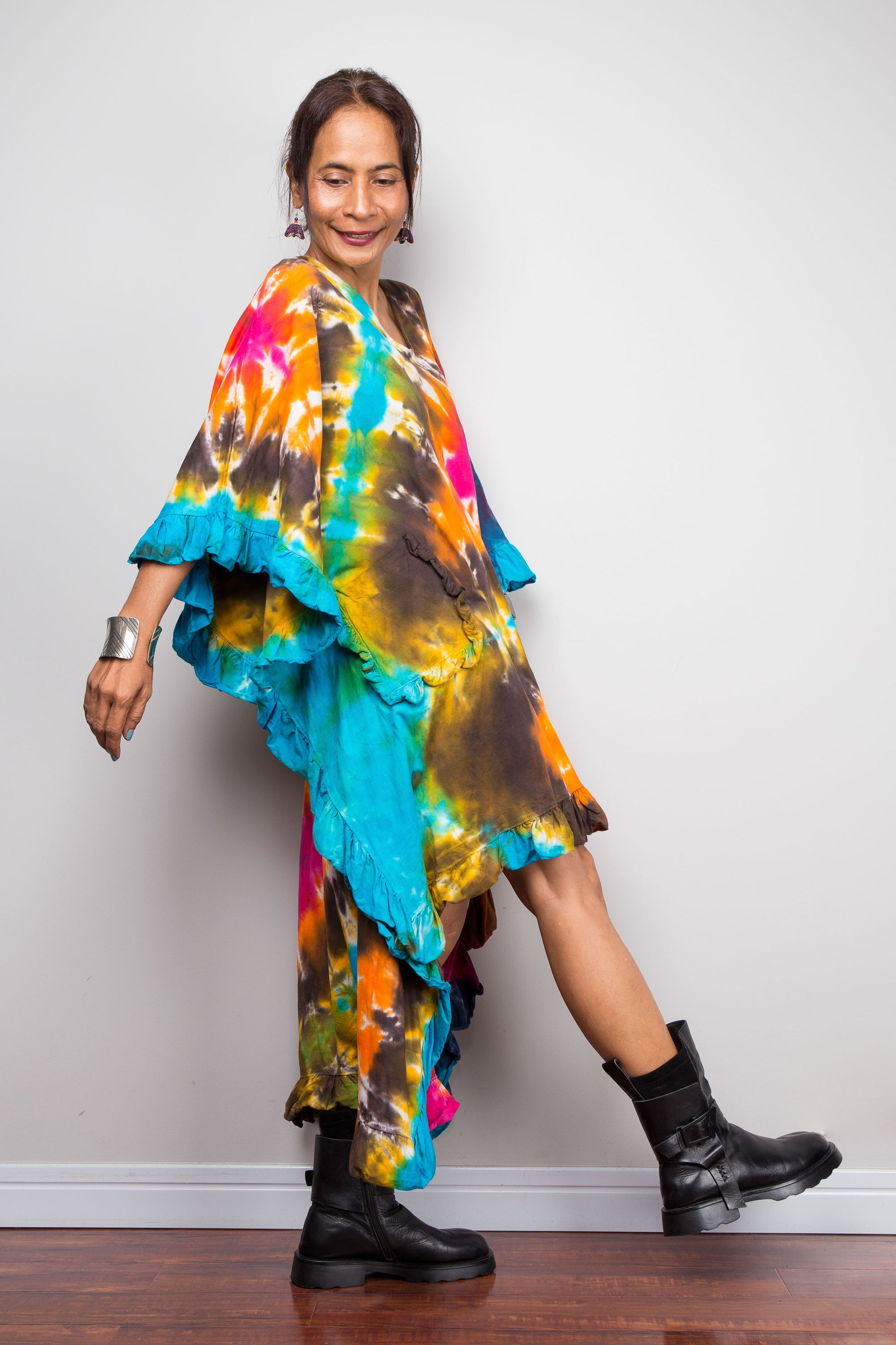A woman wearing a vibrant, multicolored tie-dye kaftan tunic with a high-low hemline that is short in the front and cascades into a long train at the back