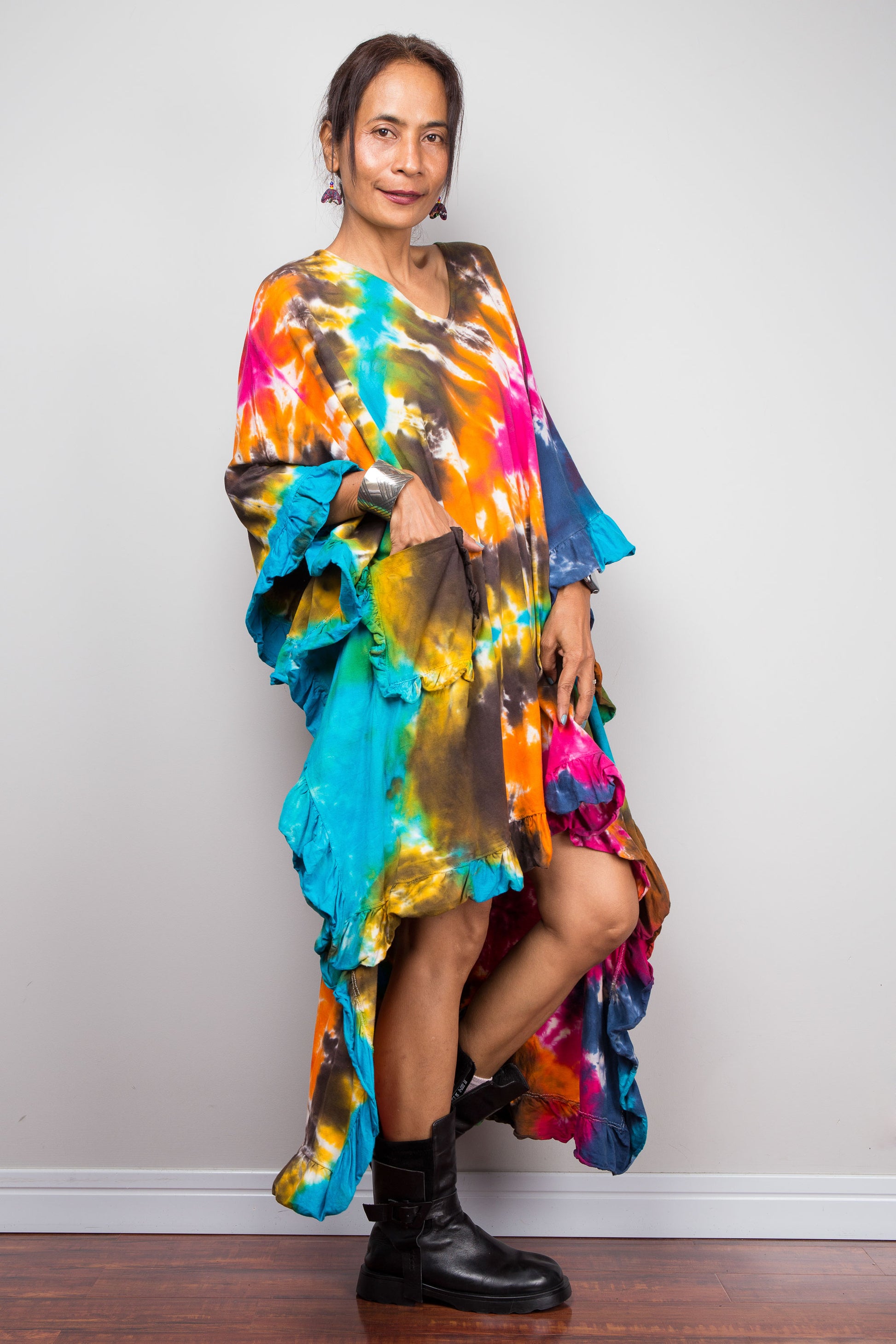 A woman wearing a vibrant, multicolored tie-dye kaftan tunic with a high-low ruffled hemline that is short in the front and cascades into a long train at the back