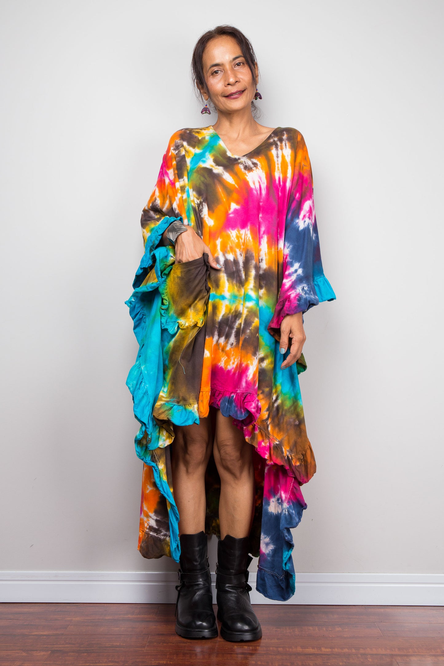 A woman wearing a vibrant, multicolored Nuichan original tie dye kaftan tunic with a high-low ruffled hemline that is short in the front and cascades into a long train at the back