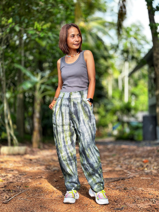 Model wearing Nuichan tie-dye hemp pants in a gray-green shade, crafted from handwoven Hmong hill tribe fabric. These boho hemp trousers, with their loose fit and four pockets, are styled with a simple top.