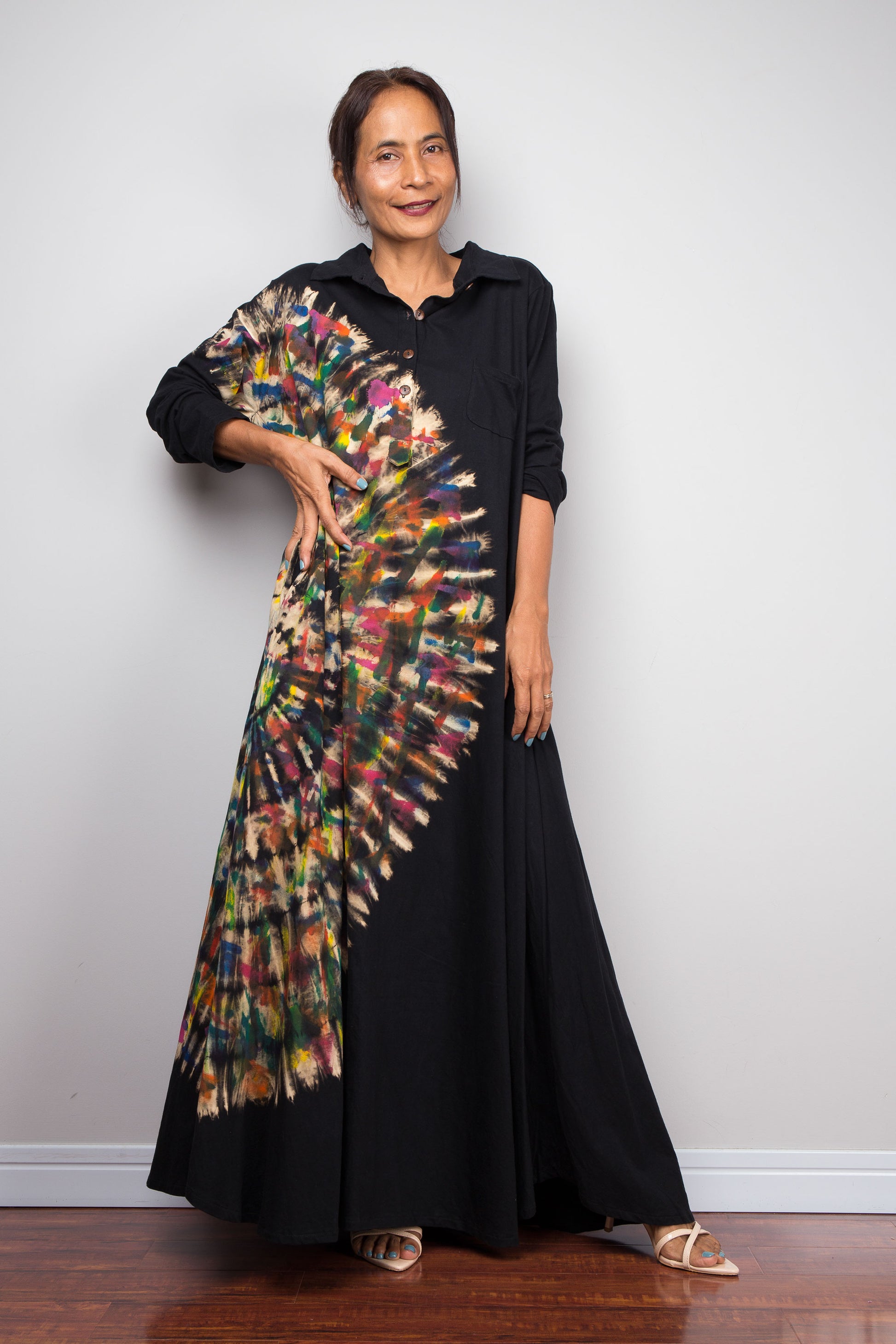 Front of woman in black long-sleeve tie dye maxi shirt dress. An asymmetric, vibrant hand-dyed multi-color tie-dye sunburst sweeps diagonally across the front. 
