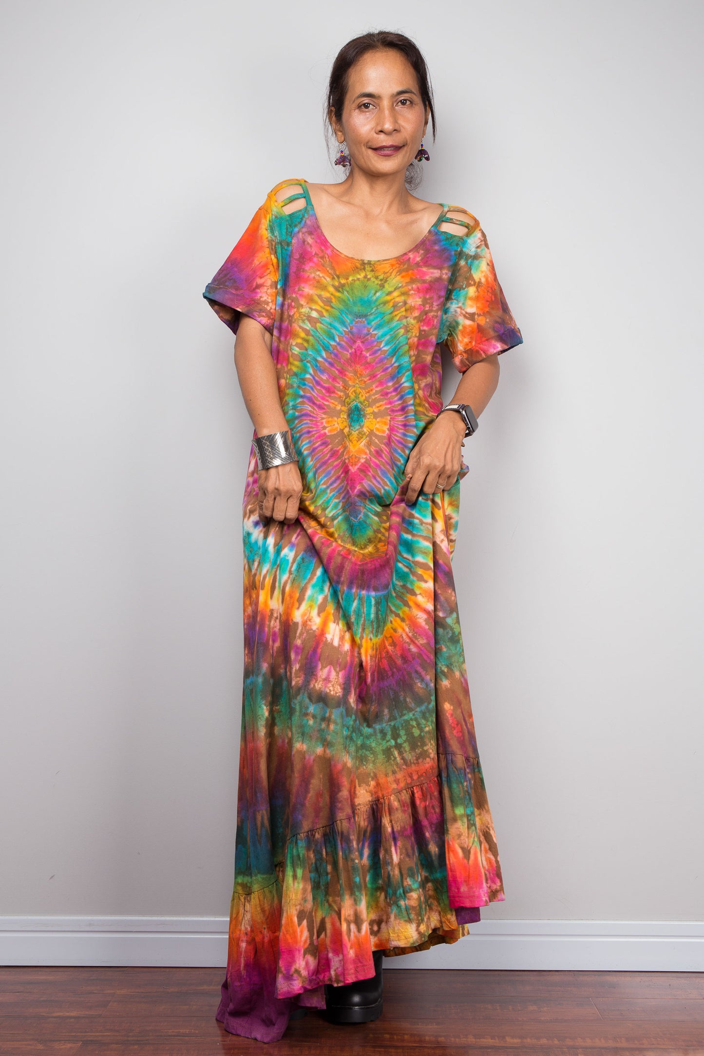 Front-facing view of a model wearing the Nuichan rainbow tie dye maxi dress, showcasing the full-spectrum starburst pattern radiating from a central teal diamond, scoop neckline, short sleeves with cut-out ladder slash details.