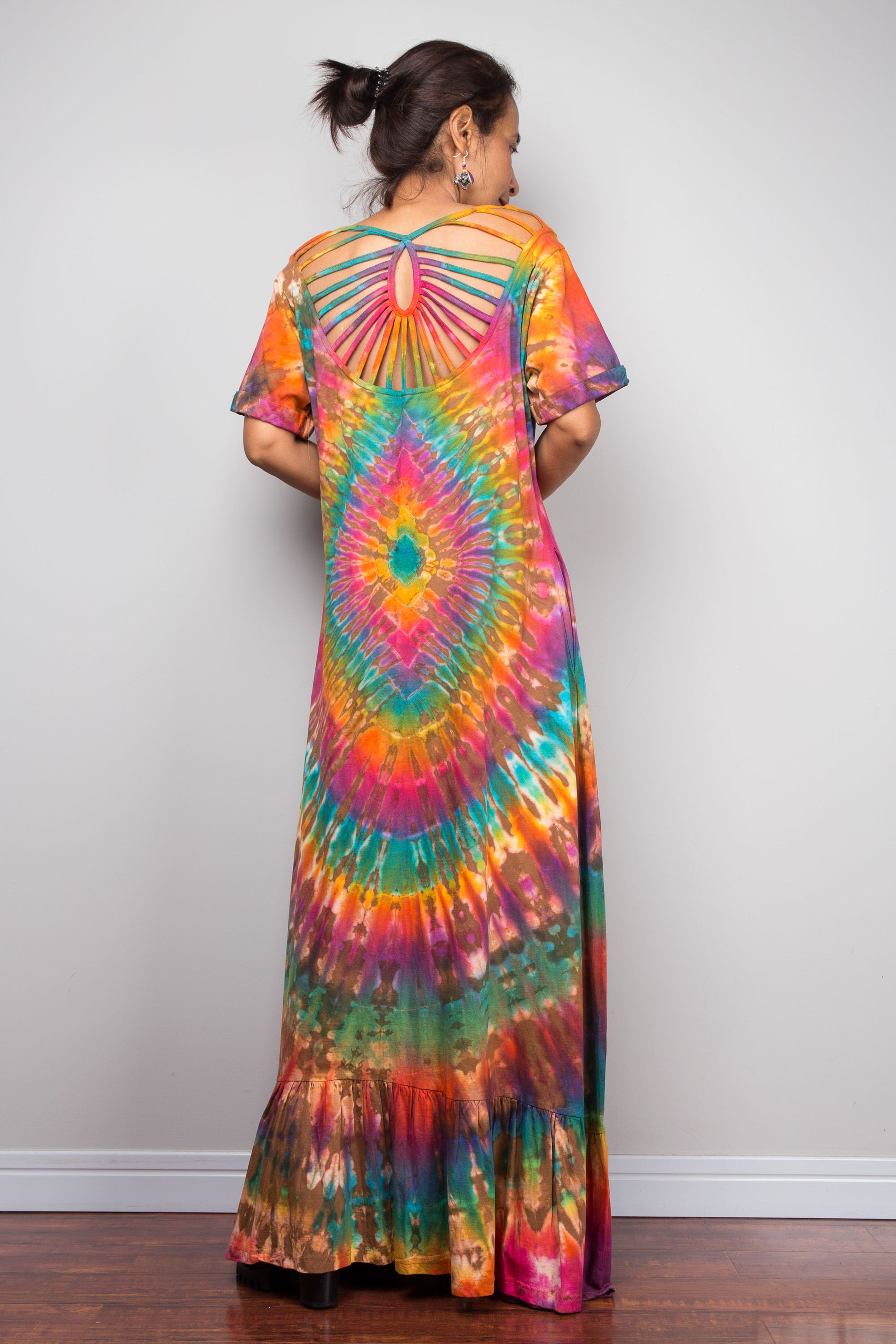 Rear view of a model in the Nuichan rainbow tie dye maxi dress, highlighting the dramatic cage-style cut-out sunburst back with rainbow-dyed fabric strips radiating from a central keyhole, full-spectrum starburst pattern.