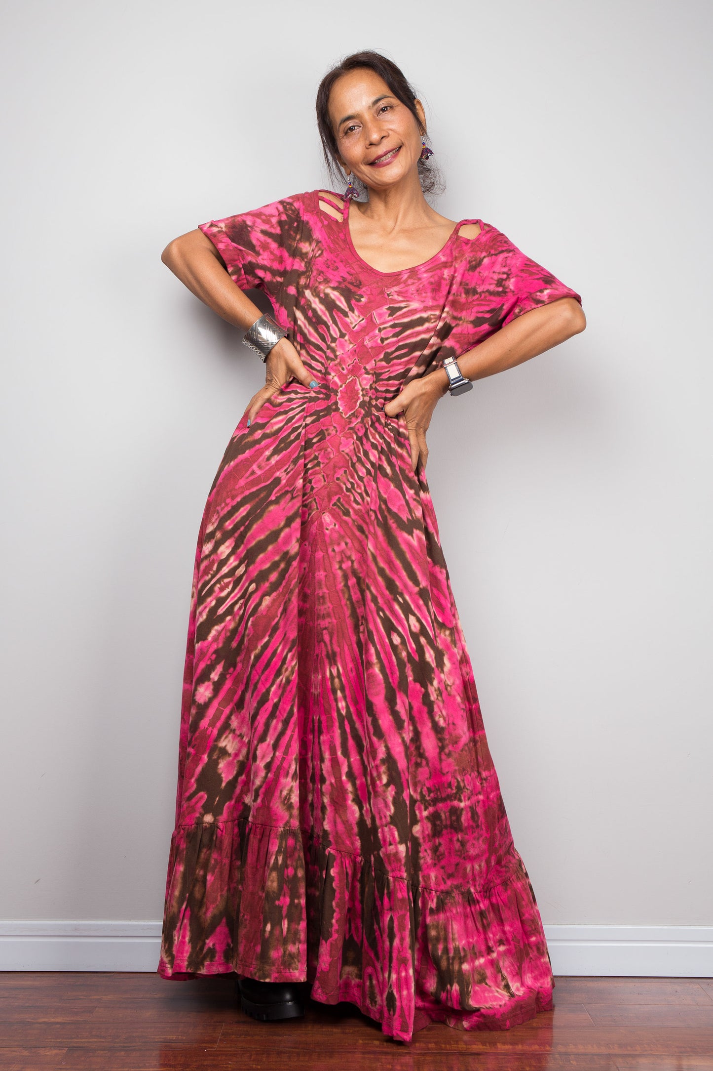 Full front view of a model in the Nuichan pink tie dye maxi dress with hands on hips, highlighting the dramatic starburst radiating from a central diamond point, relaxed A-line silhouette, cut-out shoulder details, and floor-length hem.