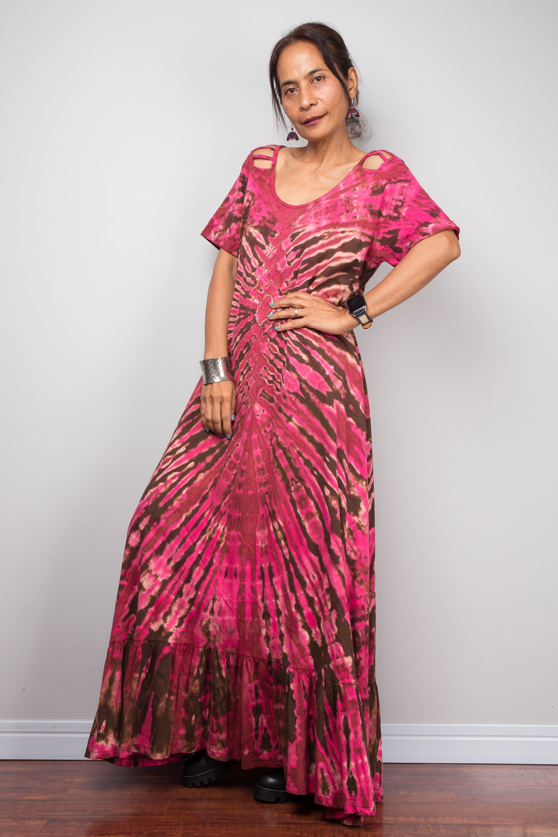Three-quarter front view of a model in the Nuichan pink tie dye maxi dress, highlighting the dramatic starburst radiating from a central diamond point, relaxed A-line silhouette, cut-out shoulder details, and floor-length hem.