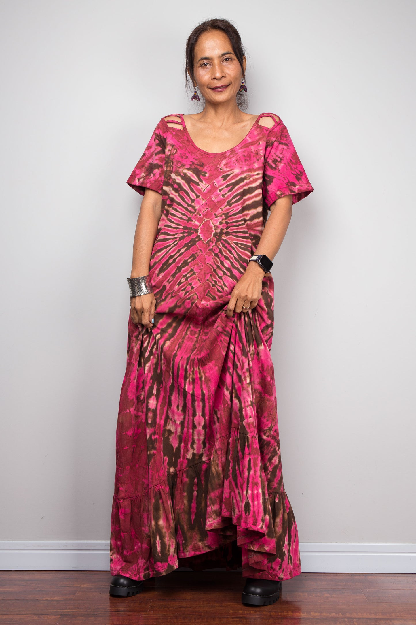 Front-facing view of a petite model wearing the Nuichan pink and brown tie dye maxi dress with hands in side pockets, showcasing the bold hot pink and chocolate brown starburst pattern, scoop neckline, short slashed sleeves.