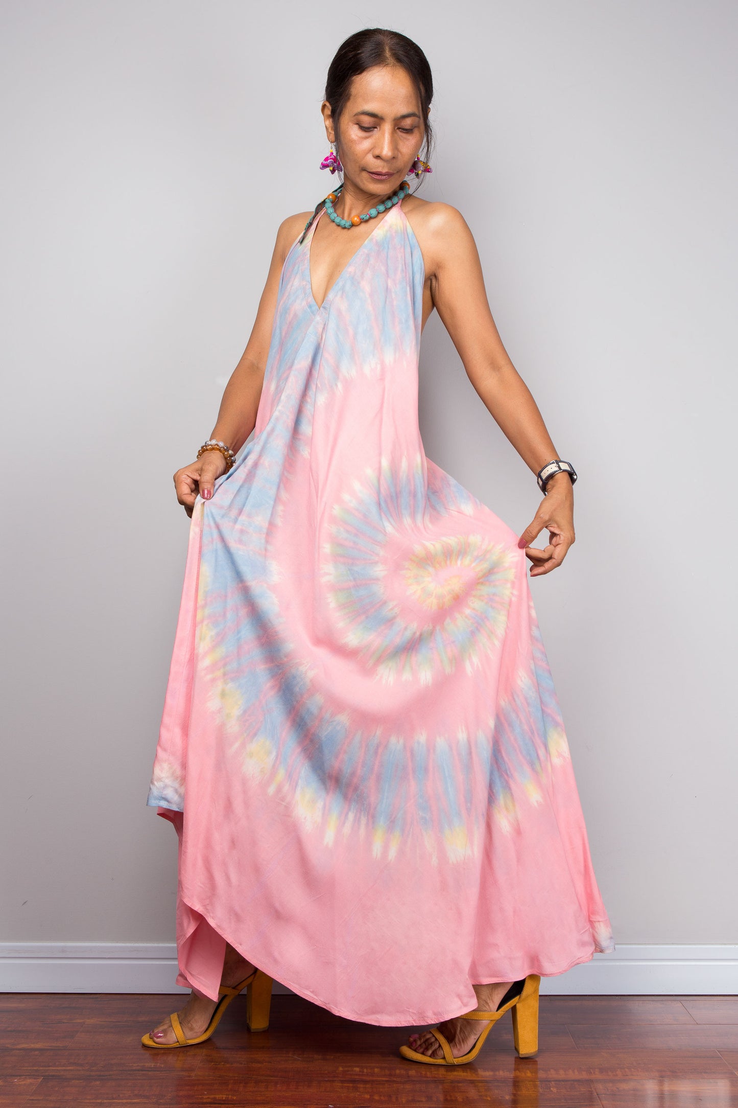 Woman wearing a tie dye maxi dress with pink and blue patterns against a plain background