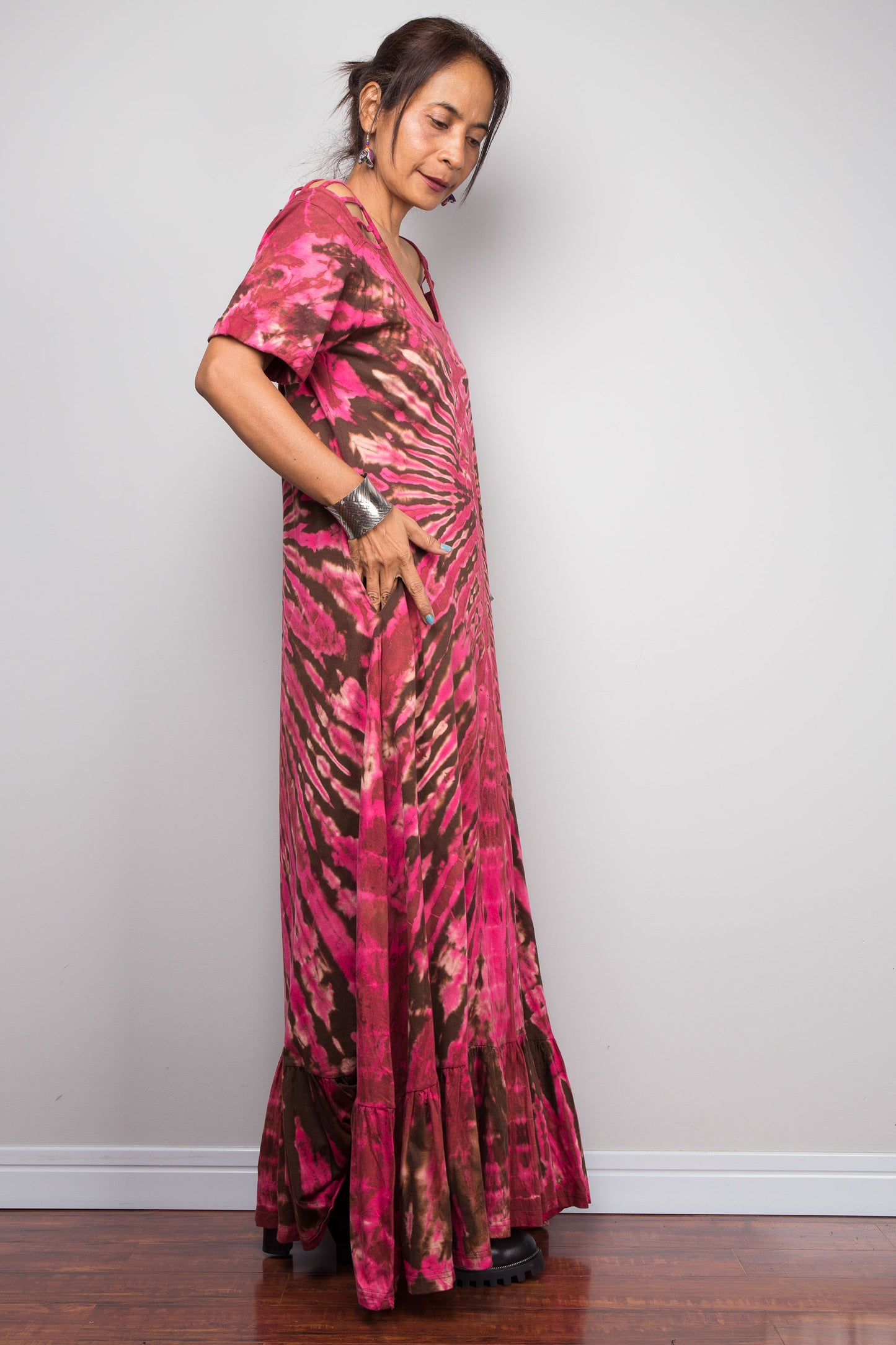 Sideview of a model in the Nuichan pink tie dye maxi dress with hand in pocket, highlighting the dramatic starburst radiating from a central diamond point, relaxed A-line silhouette, cut-out shoulder details, and floor-length hem.