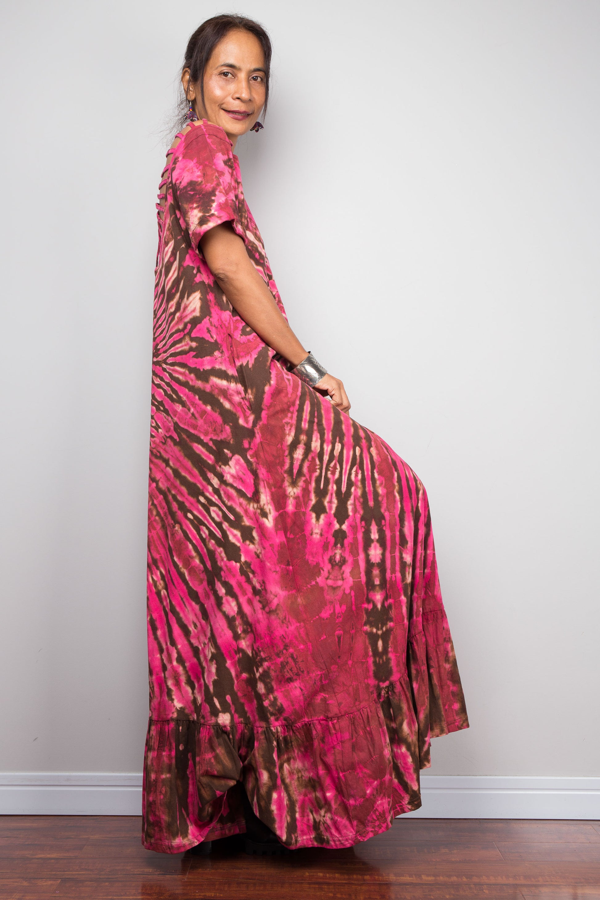 Side view of a petite model in the Nuichan pink tie dye maxi dress with hands on hips, highlighting the dramatic starburst radiating from a central diamond point, relaxed A-line silhouette.