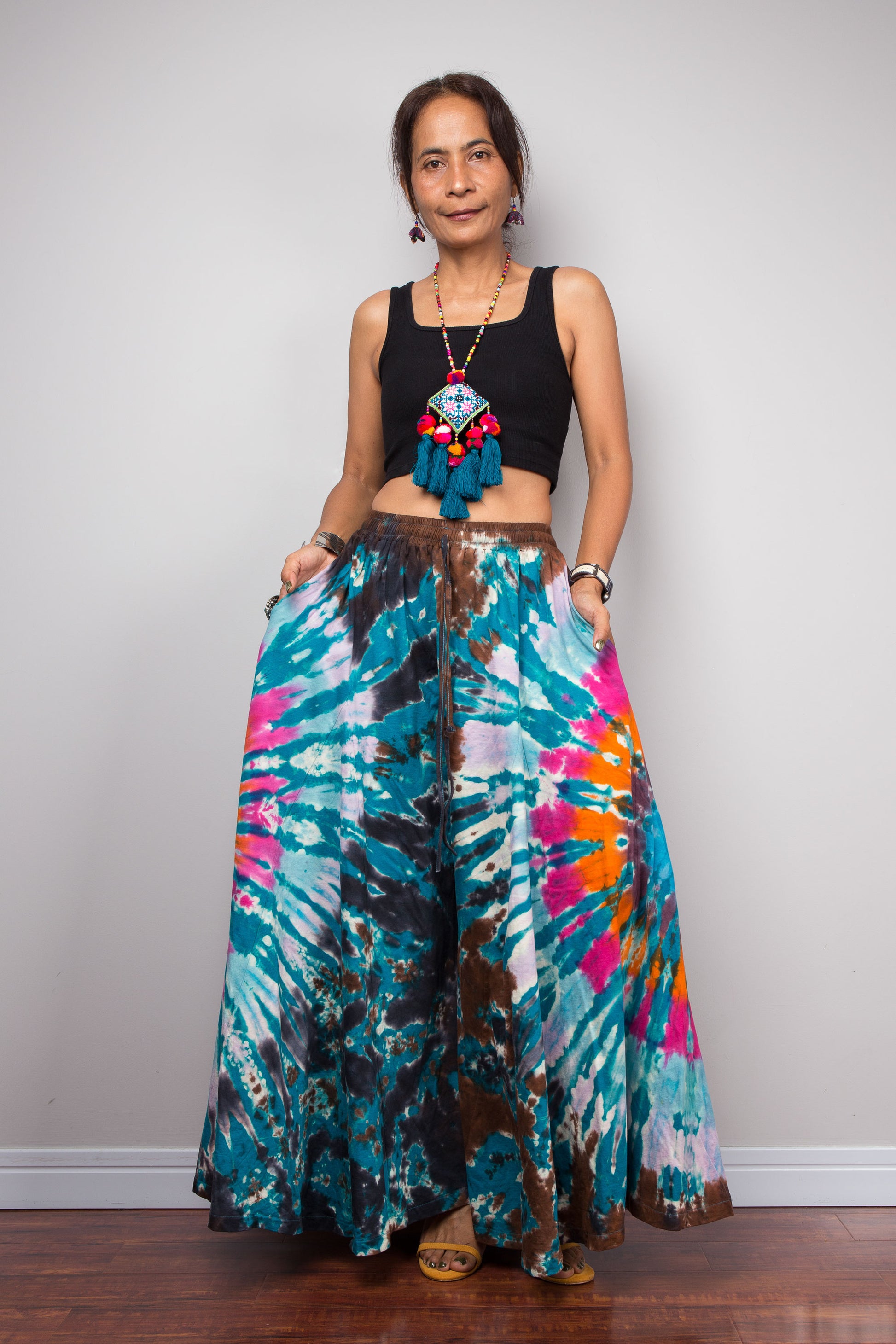 Hero front view of a model wearing the Nuichan multicolour tie dye wide leg palazzo pants styled high-waisted with a black crop top, showcasing the full dramatic ultra-wide leg silhouette and vibrant teal turquoise pink and orange freeform starburst hand-dyed pattern