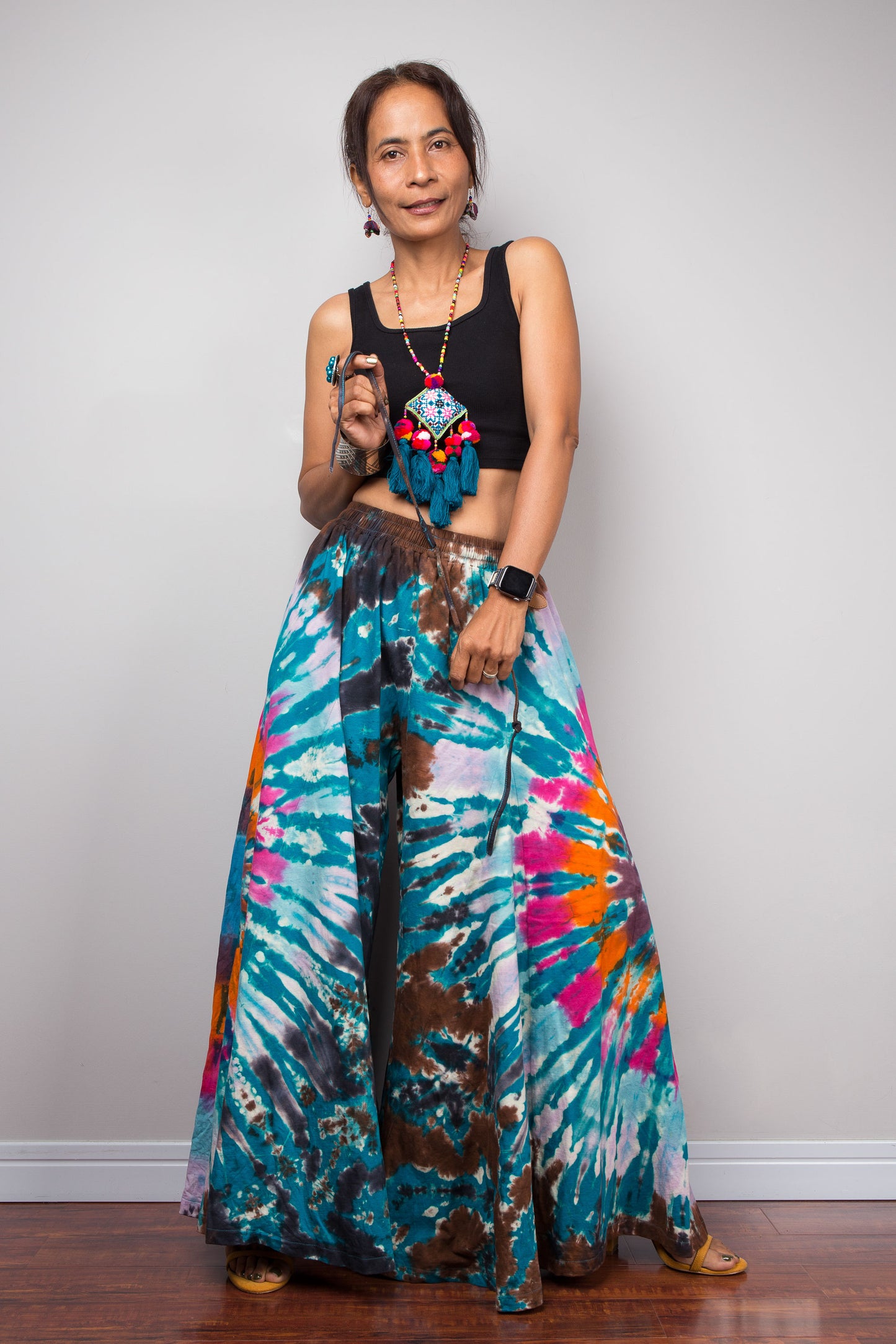 Dynamic movement shot of a model in the Nuichan multicolour tie dye palazzo pants, capturing the immense sweeping volume and skirt-like fluid drape of the ultra-wide cotton legs in motion, with the vivid multicolour tie dye pattern catching the light