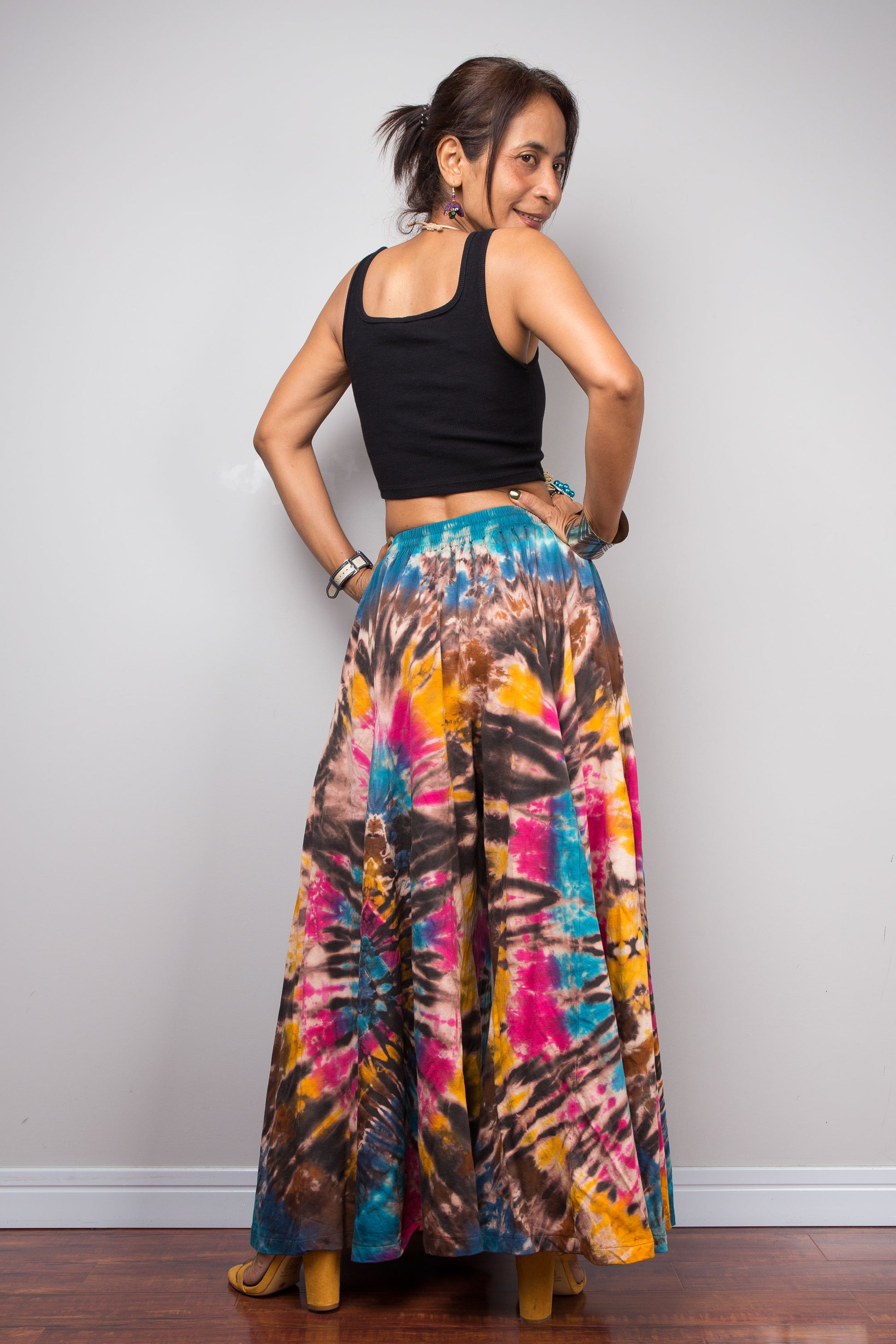 Rear view of a model wearing the Nuichan turquoise, fuchsia and golden marigold tie dye wide leg palazzo pants, highlighting the full sweeping palazzo silhouette, striking spiral tie dye artwork that continues across the back, comfortable smocked waistband, and relaxed bohemian fit.