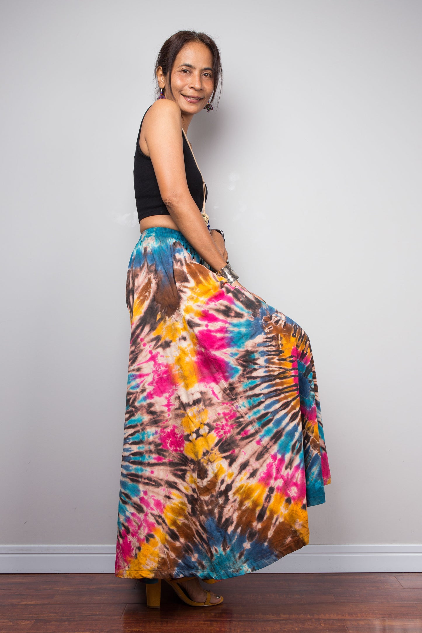 Side profile of a model wearing the Nuichan hand-dyed wide leg palazzo pants in turquoise, fuchsia and marigold spiral tie dye, showcasing the dramatic volume, fluid wide-leg cut, lightweight fabric, and flattering high-waisted silhouette.