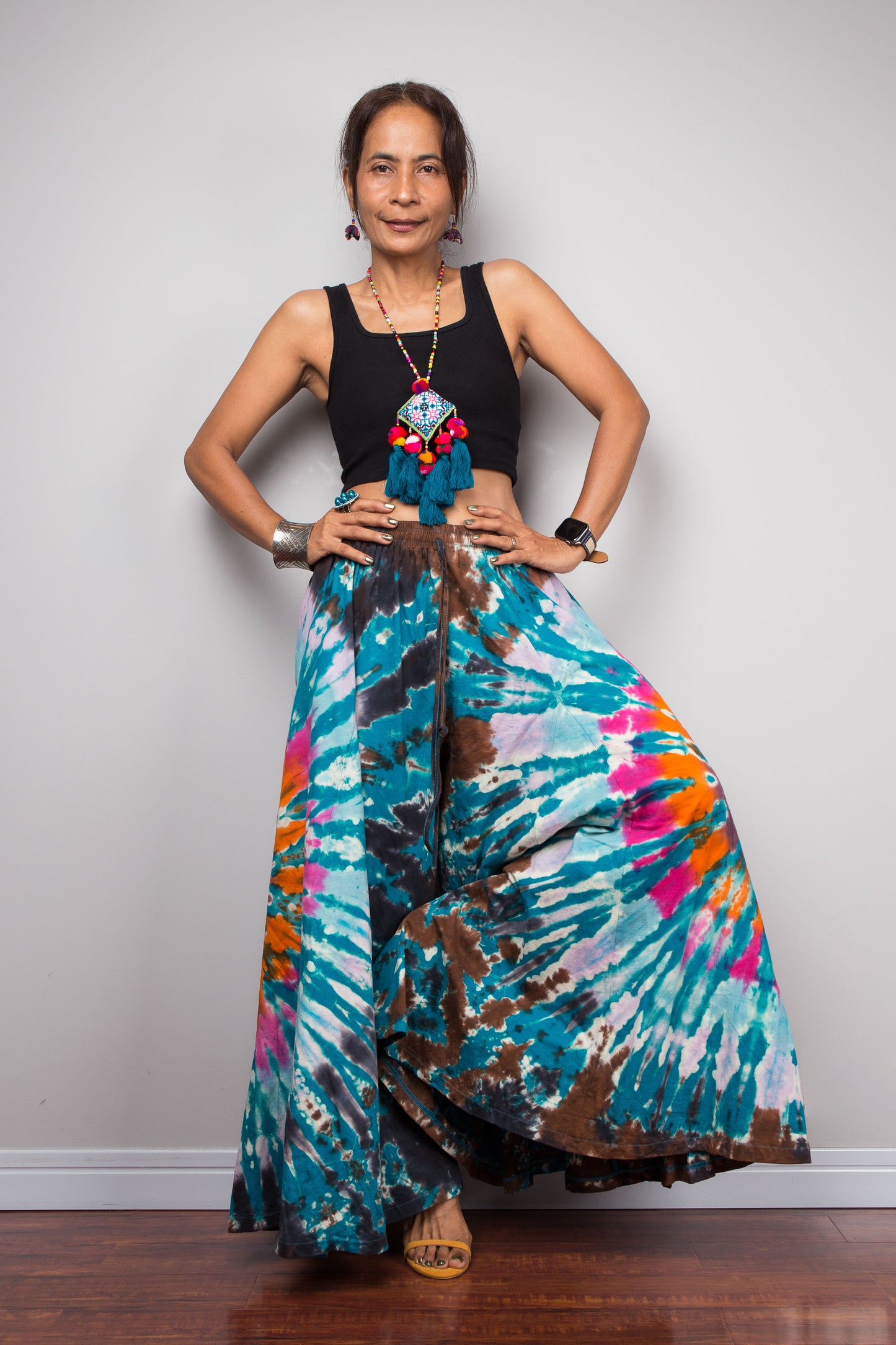 Dynamic pose of a model wearing the Nuichan multicolour tie dye palazzo pants, showcasing the immense fabric movement and sweeping A-line drape of the ultra-wide cotton legs as they catch the air, styled with a black crop top