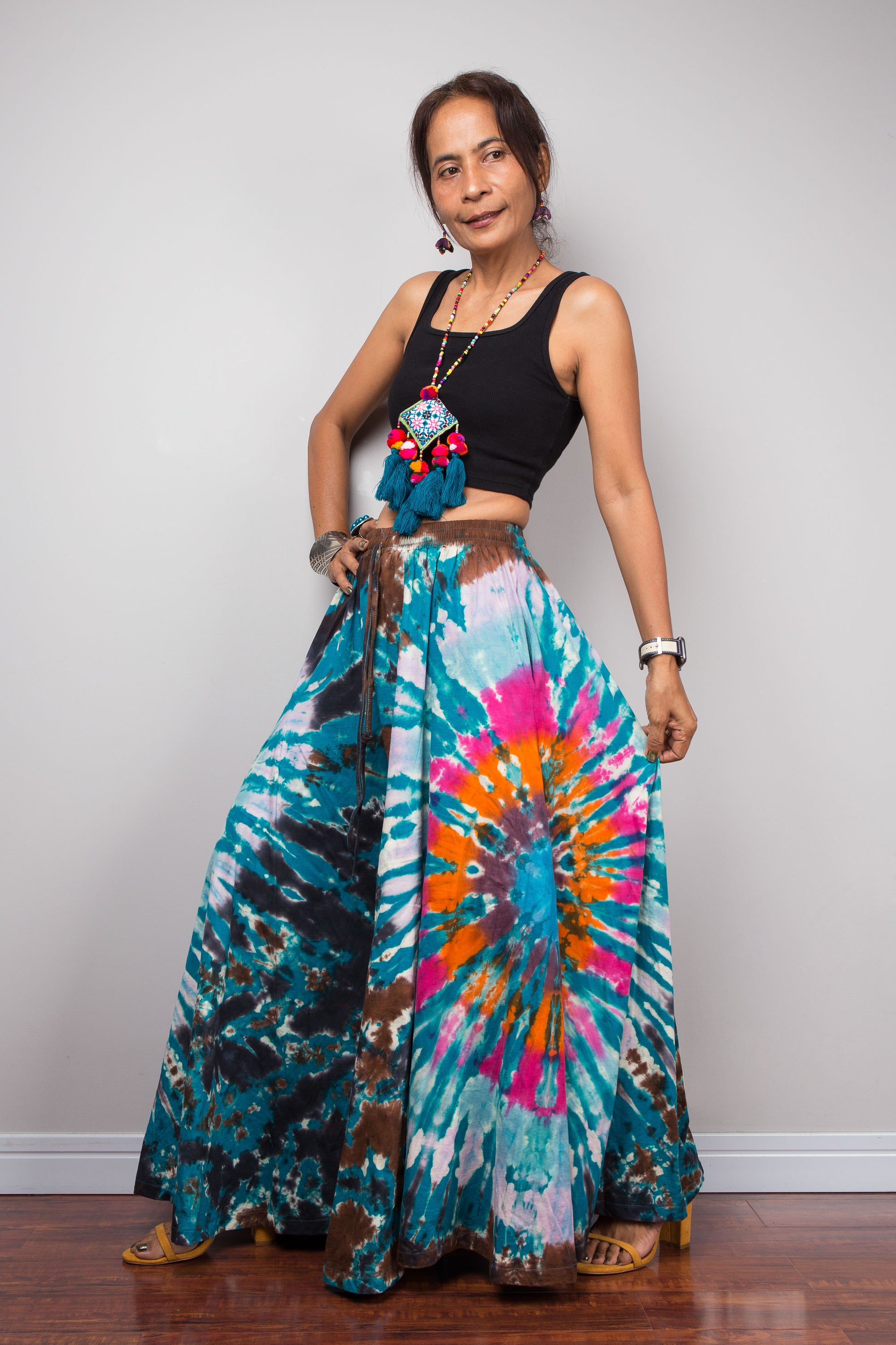Three-quarter side view of a model wearing the Nuichan multicolour tie dye palazzo pants holding out the wide leg to display the full fabric volume, bold freeform starburst tie dye in teal hot pink and orange, and functional hidden side pocket