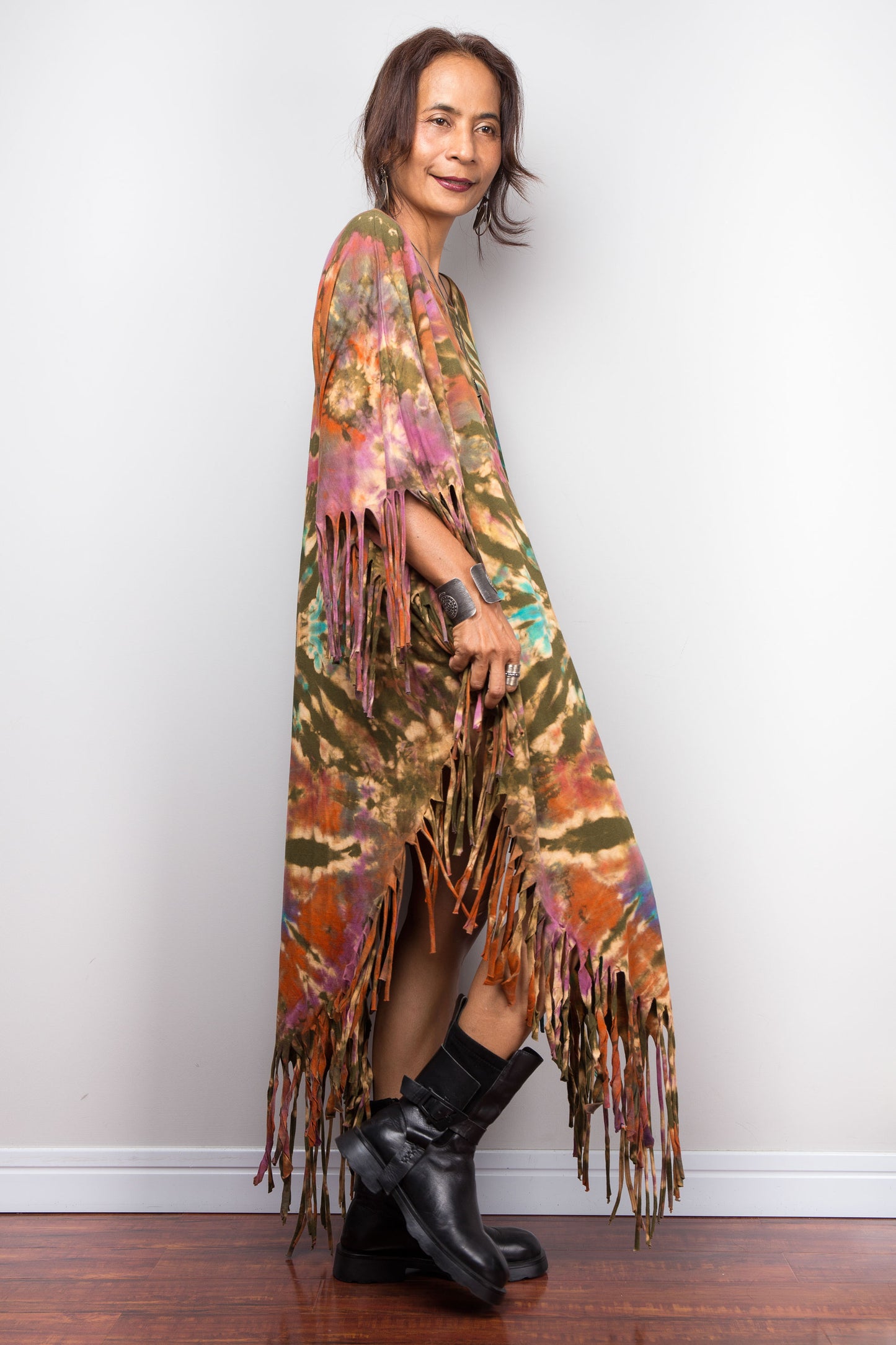 Woman wearing a colorful fringed tie dye poncho against a white wall.