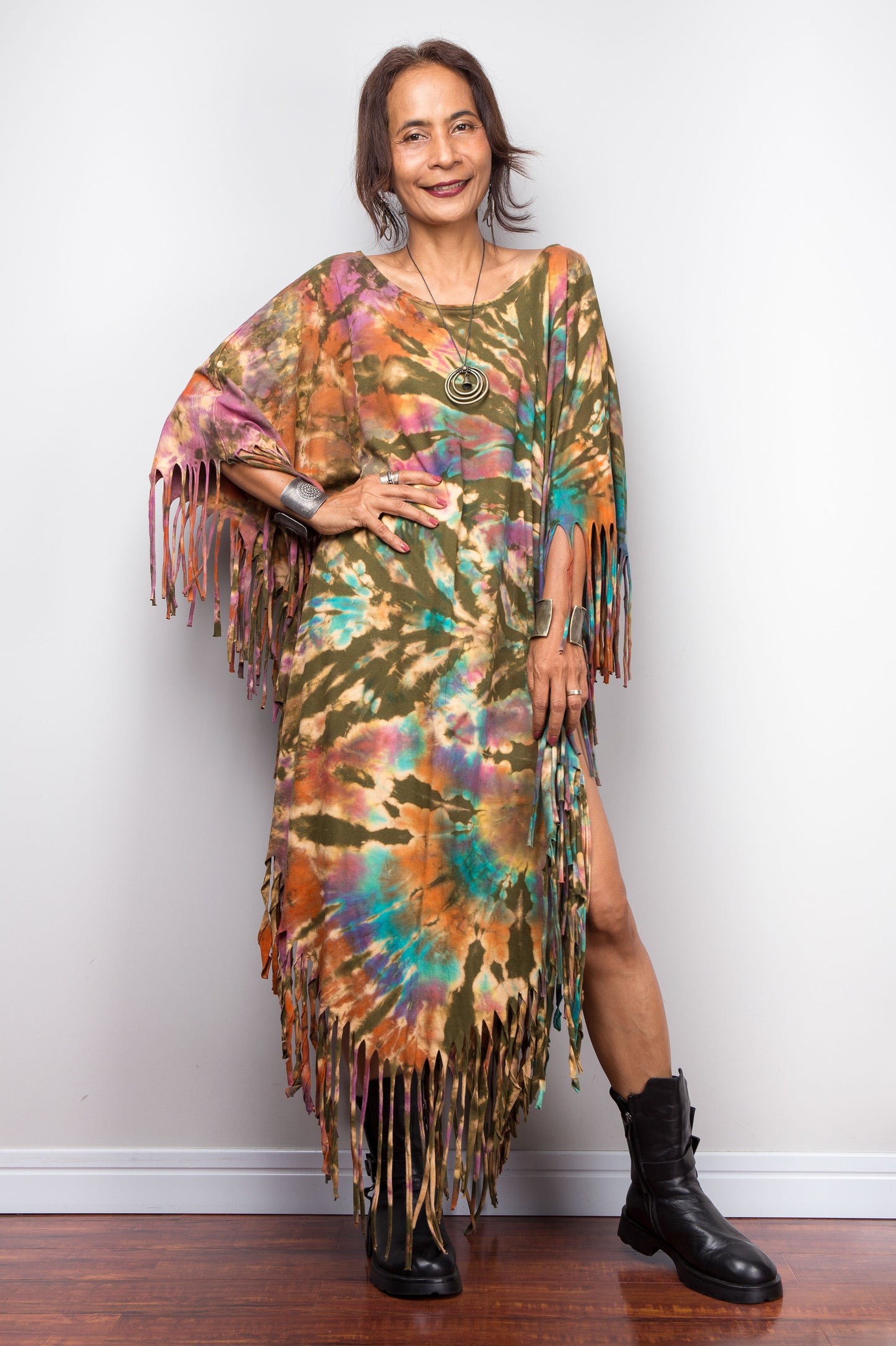 Woman wearing a boho tie dye fringe dress against a white wall.
