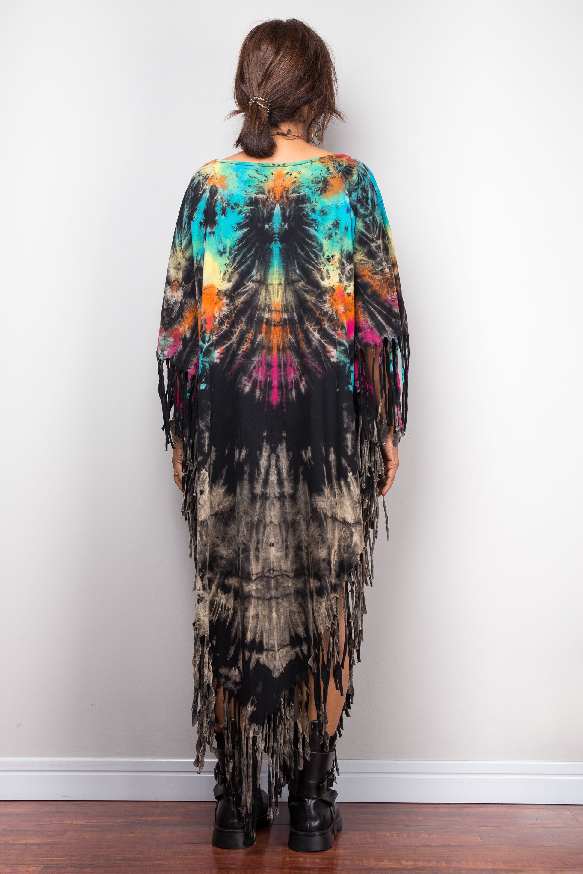 Person wearing a colorful tie-dye dress with fringe on a white background