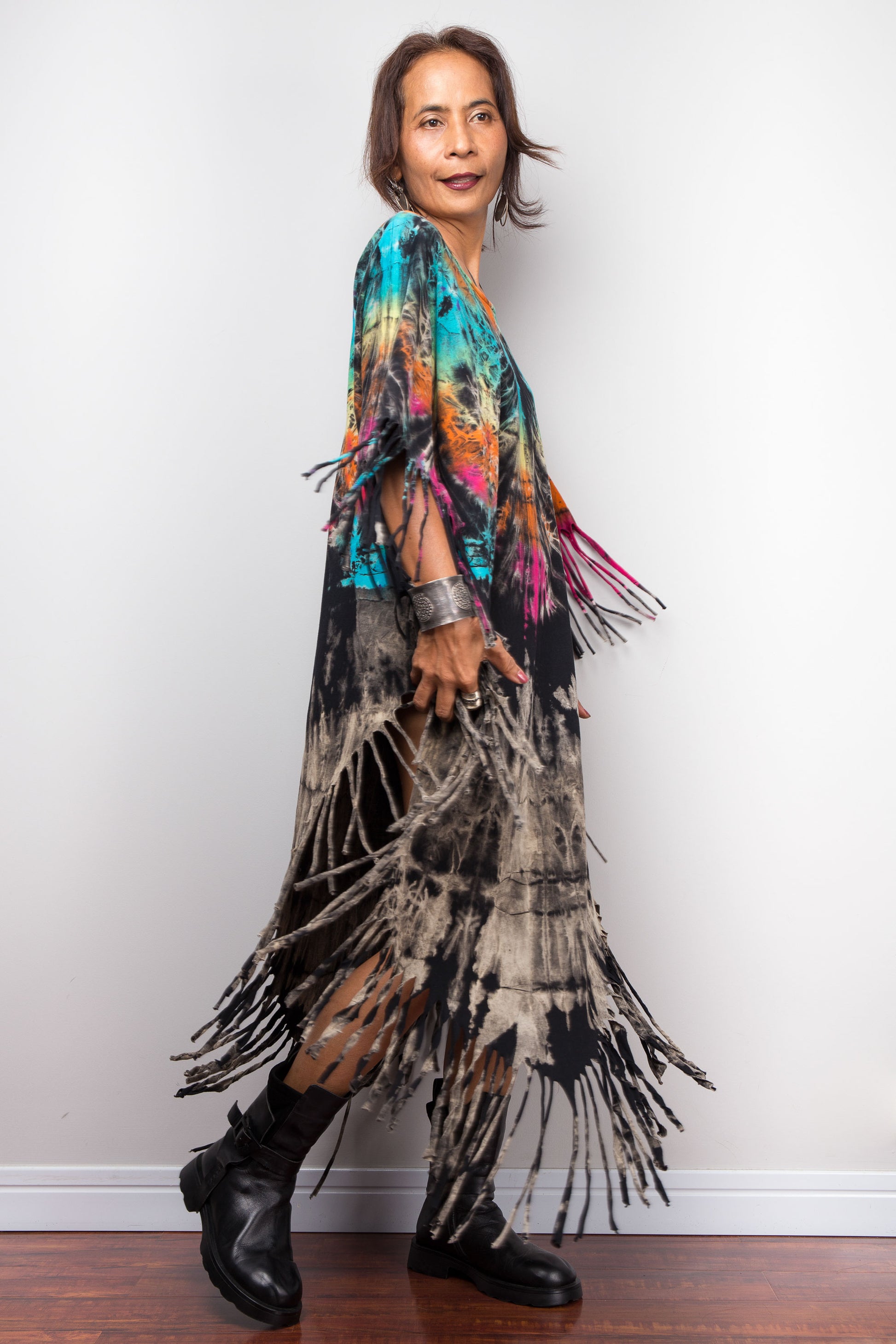 Woman wearing a colorful tie dye fringe dress against a white wall