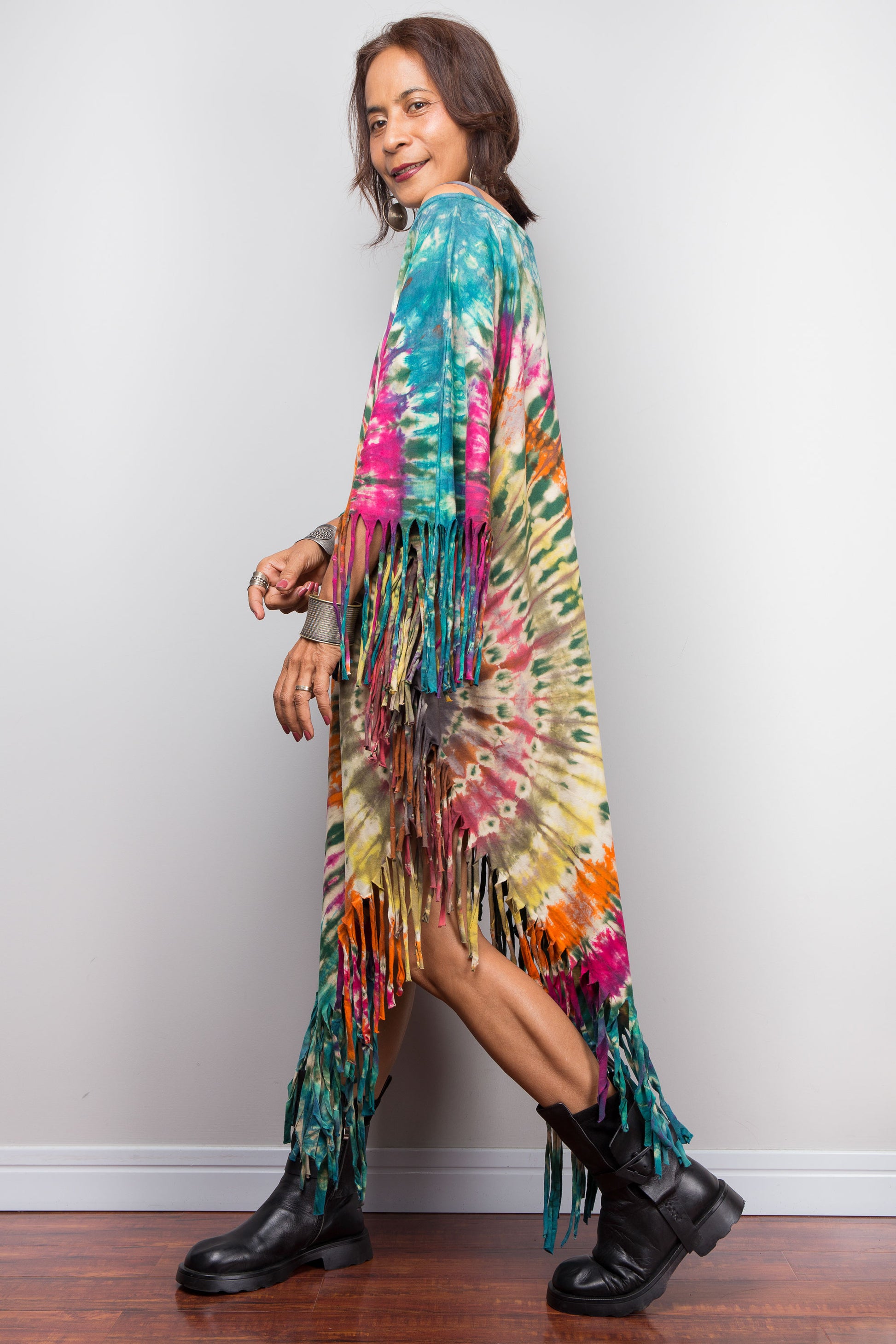 Woman wearing a colorful tie-dye kimono with fringe on a plain background