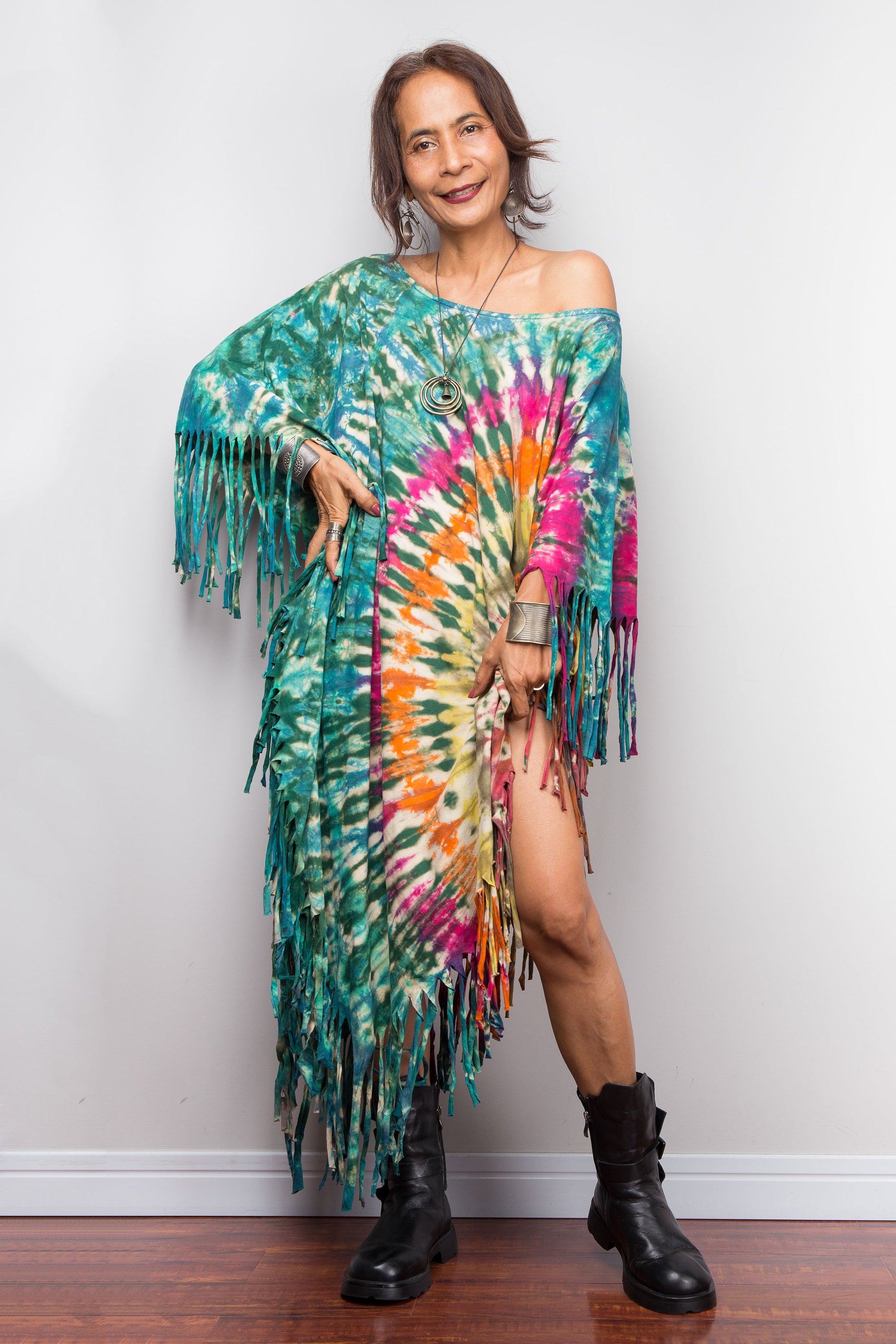 Petite woman wearing a colorful tie dye poncho dress with fringe against a plain background