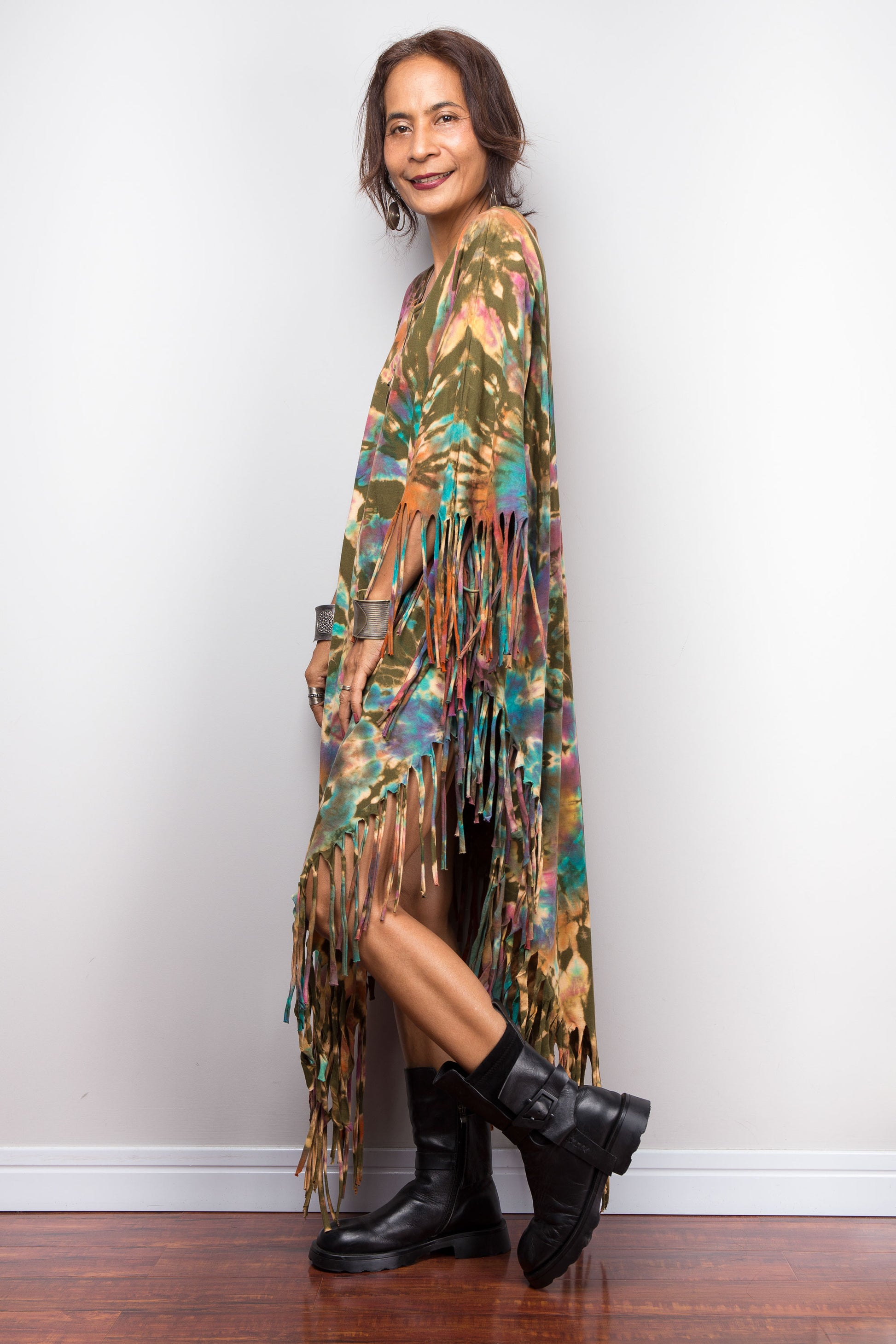 Woman wearing a tie dye fringe dress and black boots against a plain background
